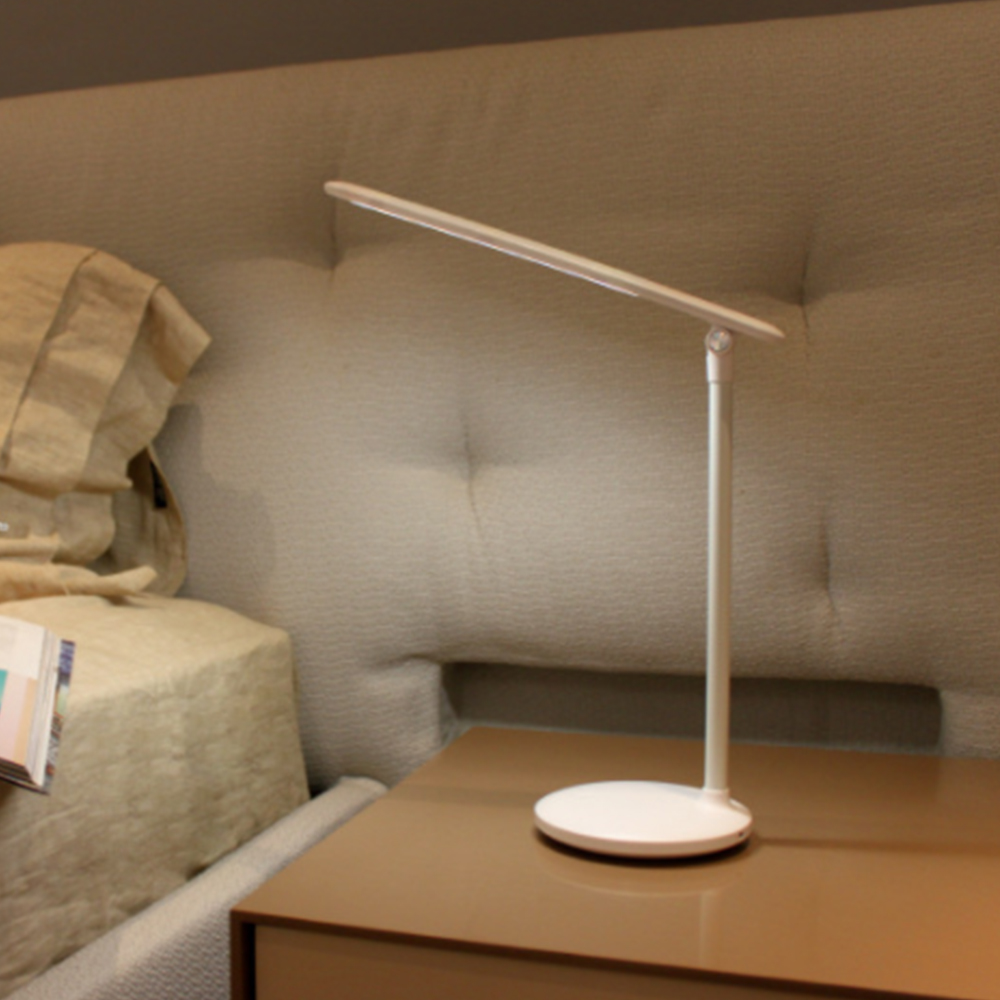 Weiße Schreibtischlampe mit dünnem, verstellbaren Arm, auf braunem Nachttisch.