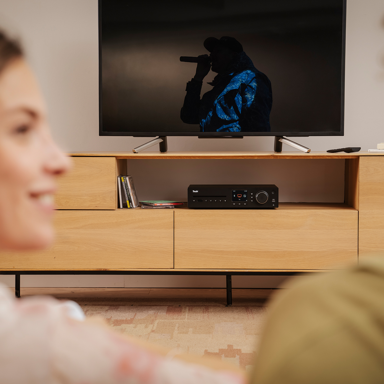 Ein Wohnzimmer mit einem Fernseher auf einem Holzschrank. Eine Person im Vordergrund schaut fern.