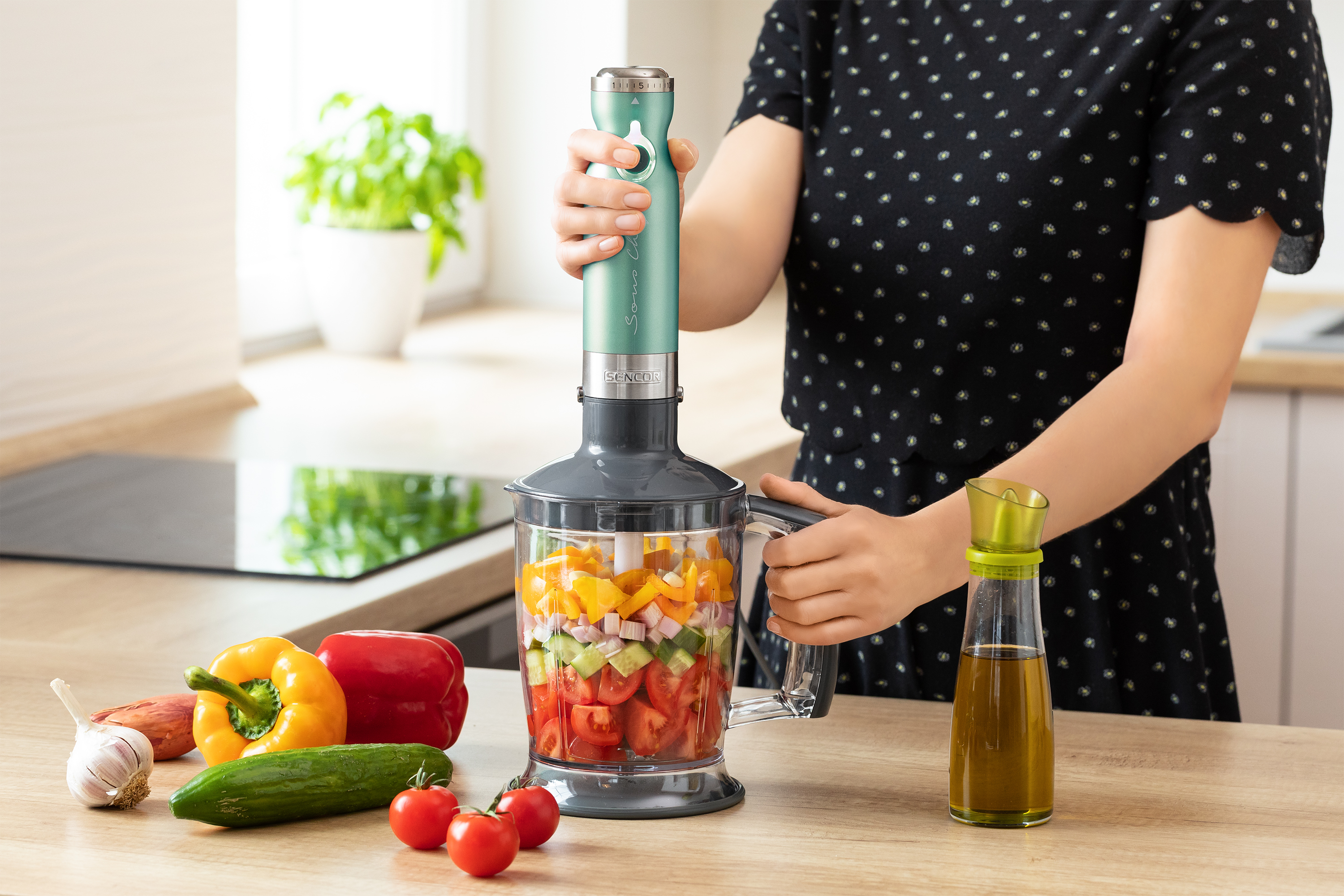 Una persona usa un frullatore a immersione per mescolare verdure in un contenitore trasparente.