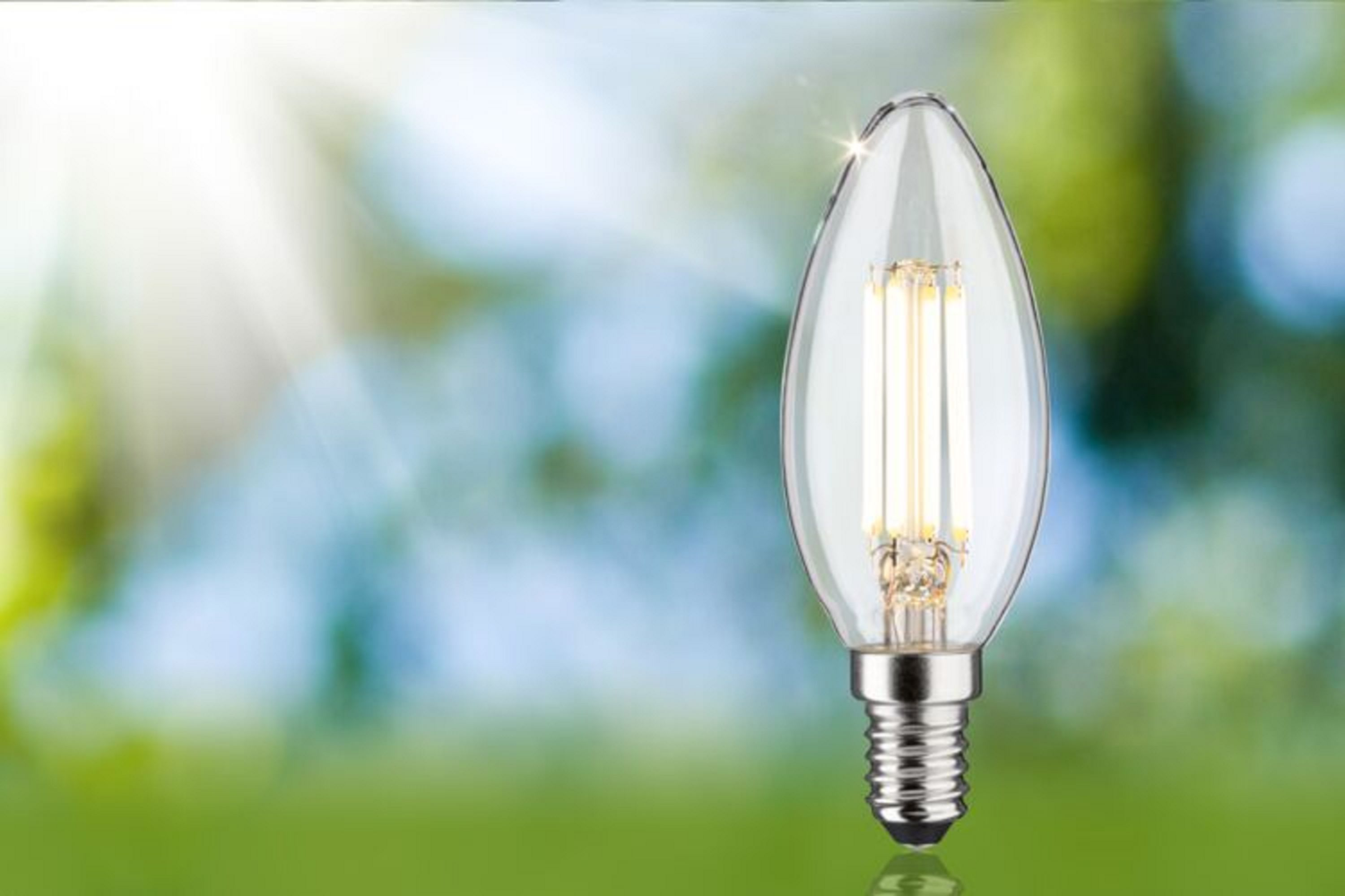 Klare, spitze LED-Glühbirne mit silbernem Sockel, beleuchtet vor verschwommenem grünen Hintergrund.
