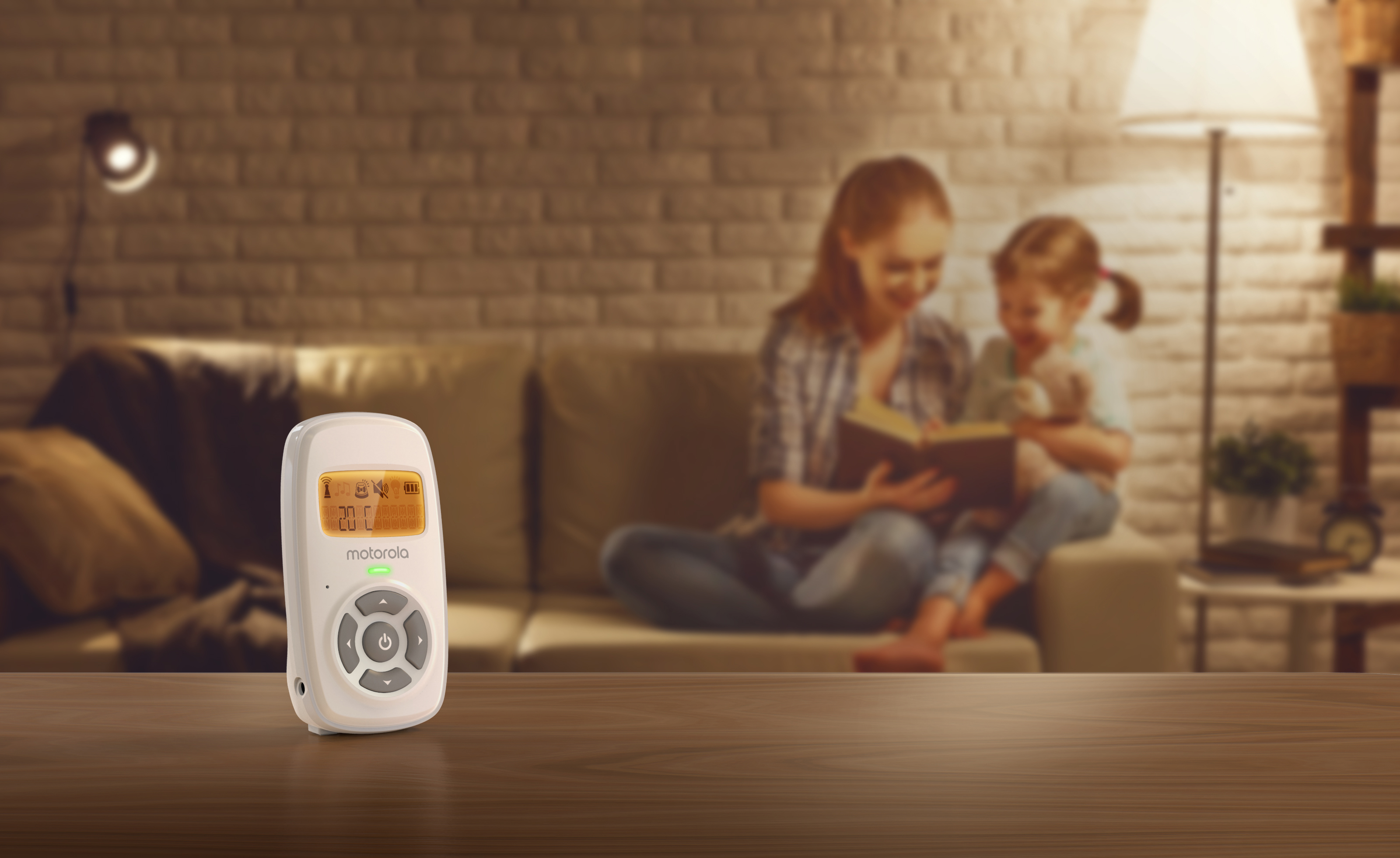 Niania elektroniczna na stole, z matką i dzieckiem czytającymi.