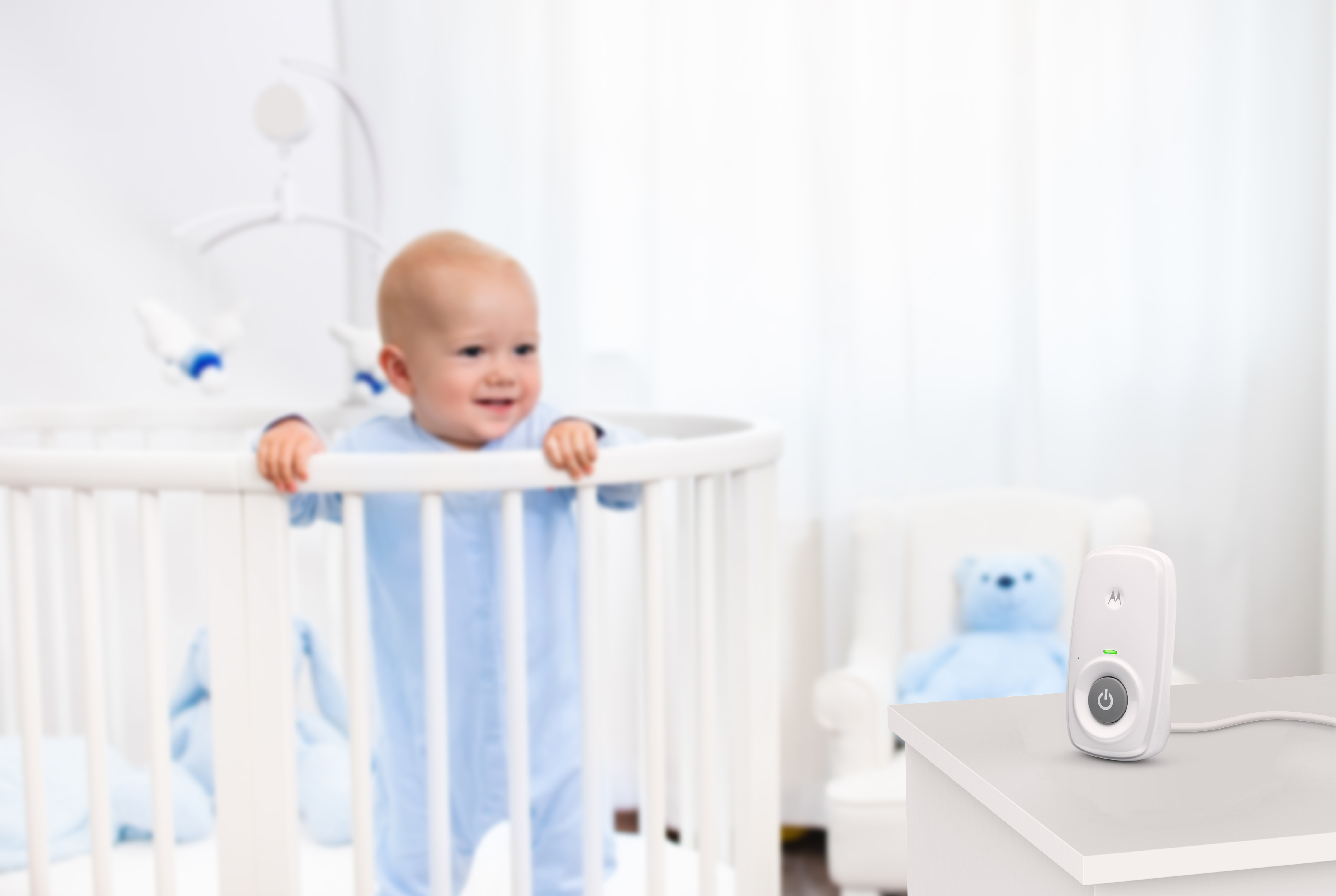 Dziecko w łóżeczku się uśmiecha. Niania elektroniczna na białym stole.