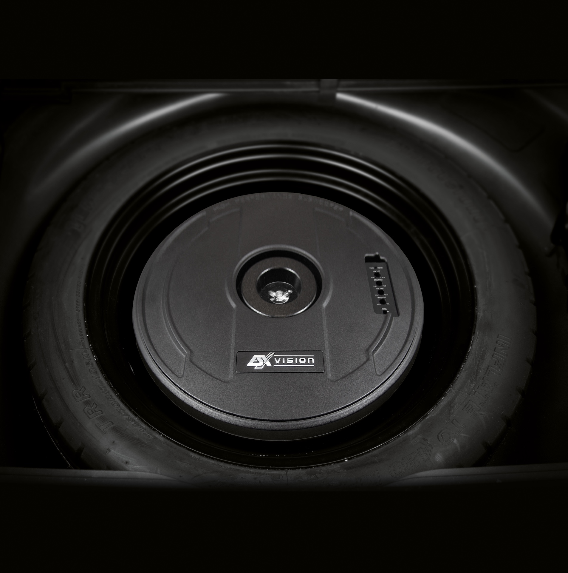 Ein Auto-Subwoofer im Reserverad. Der Subwoofer ist schwarz und trägt das Logo 'EX VISION'.