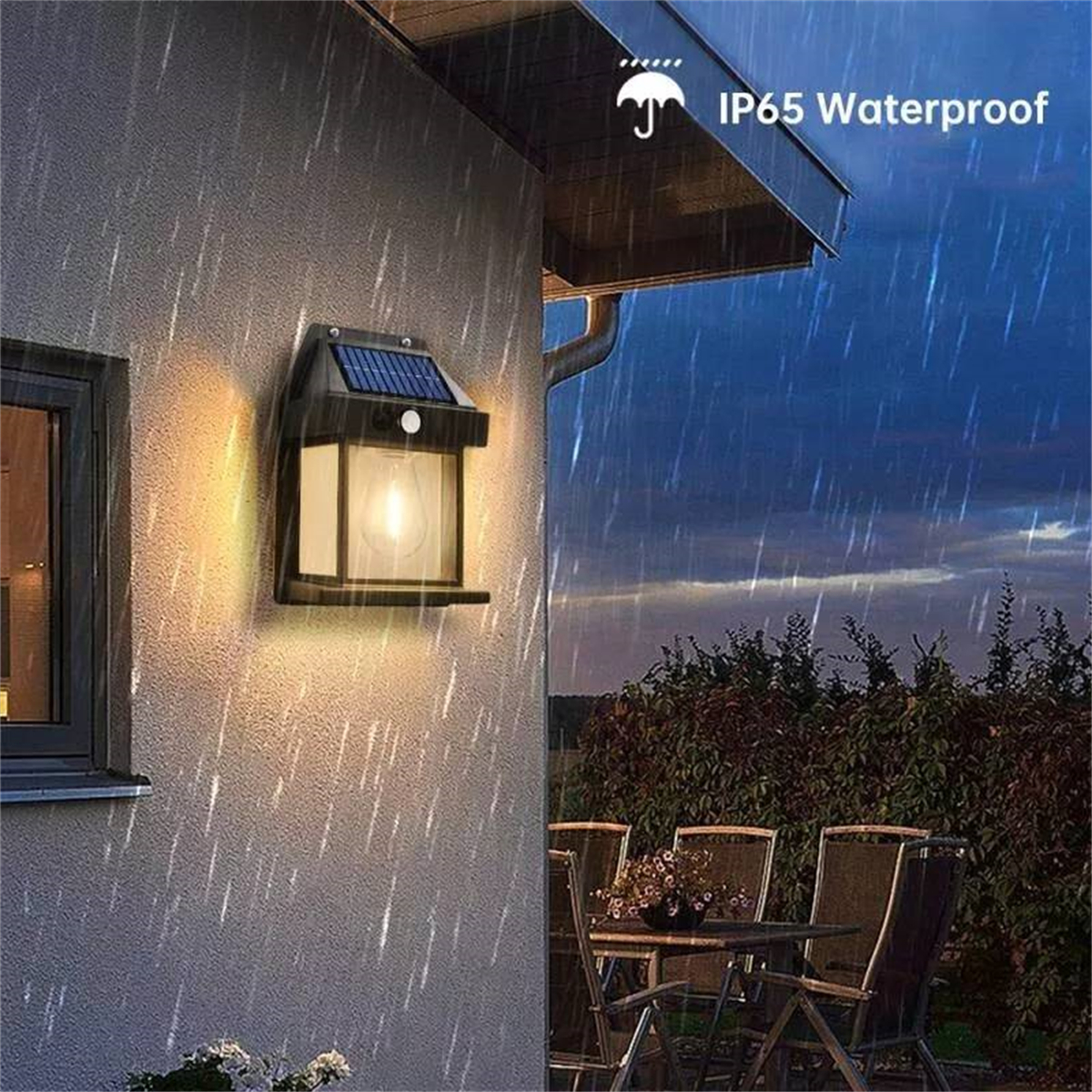 Außenwandleuchte. Es regnet. Die Lampe ist eingeschaltet. Ein Tisch und Stühle sind sichtbar.