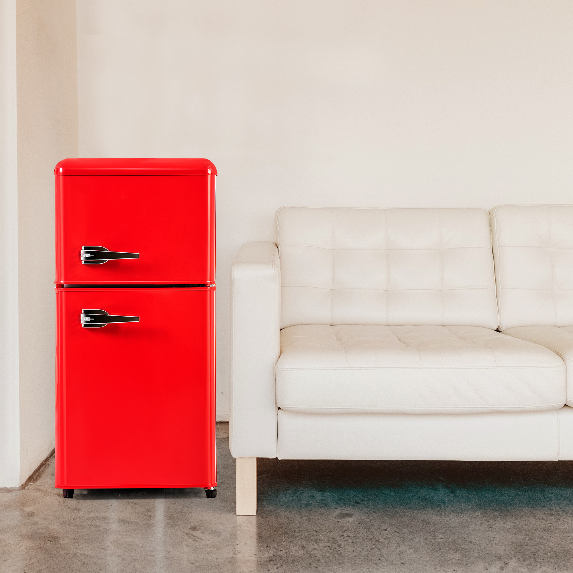 Ein roter Kühlschrank steht neben einem weißen Sofa auf grauem Betonboden.