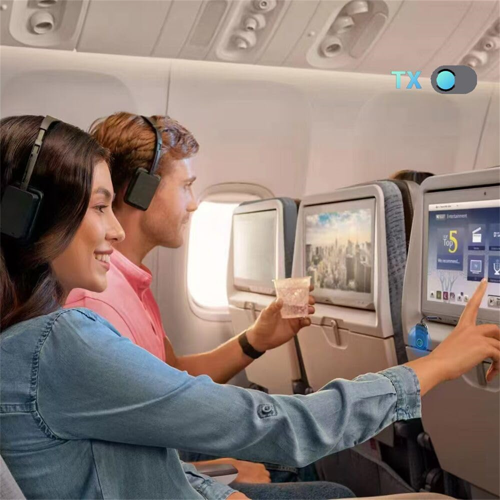 Paar im Flugzeug, schaut auf Bildschirme, trägt Kopfhörer. Die Frau zeigt auf den Bildschirm.
