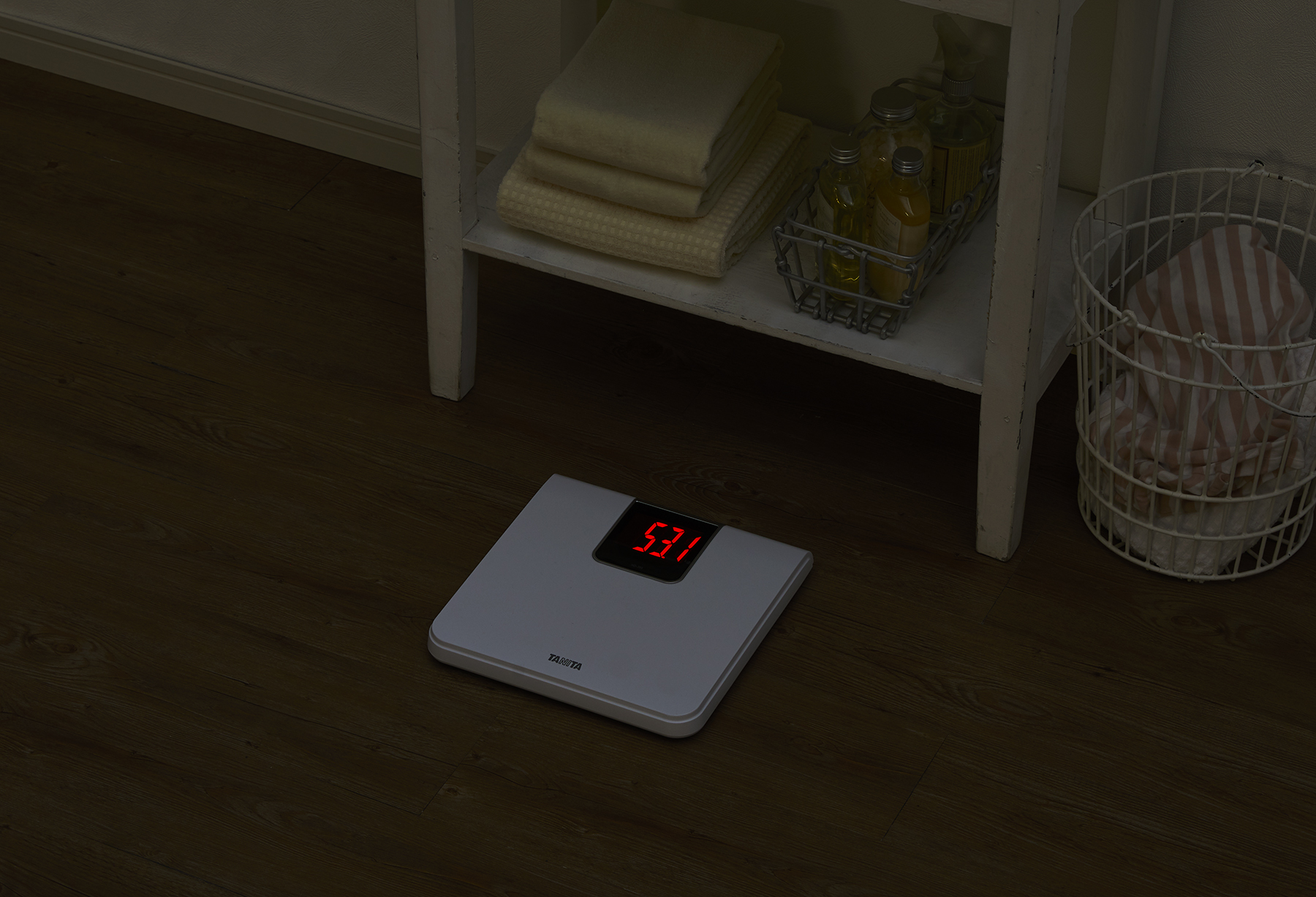 Een digitale weegschaal met 53,1, met handdoeken en een mand op de achtergrond.