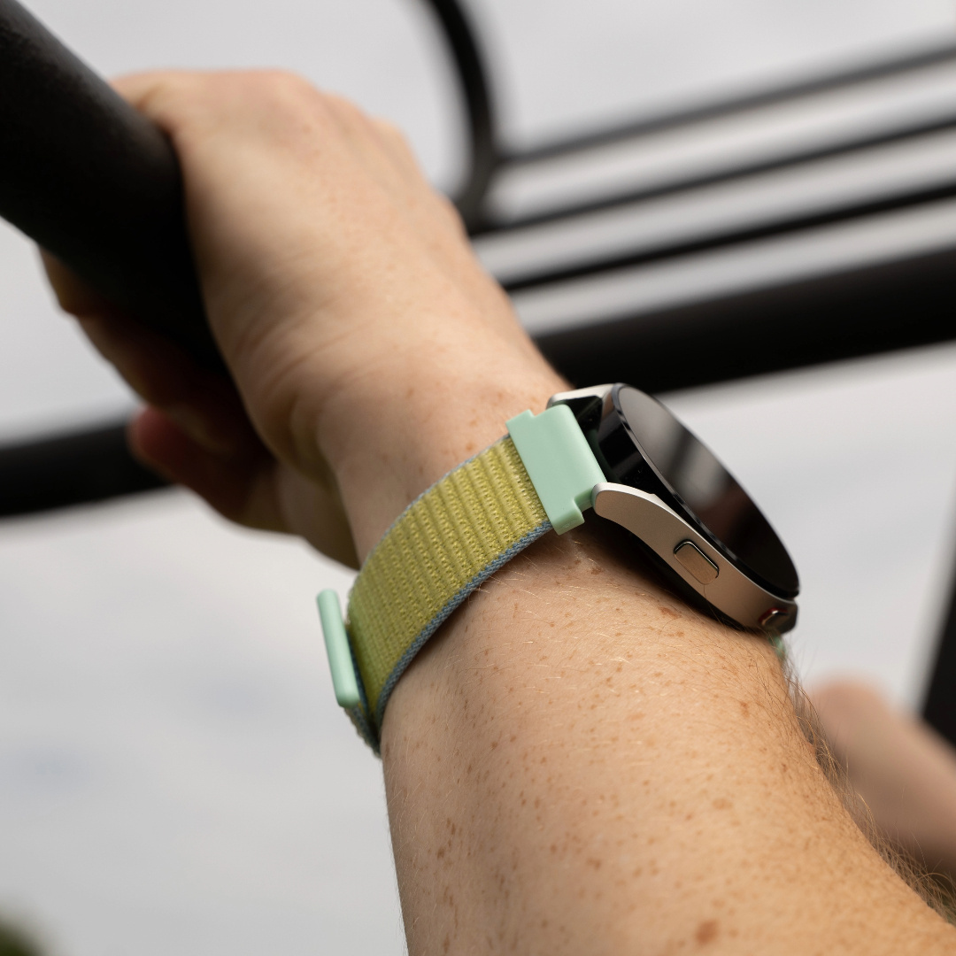 Ein Handgelenk mit einer Smartwatch, mit gelbem Armband, hält eine Stange.