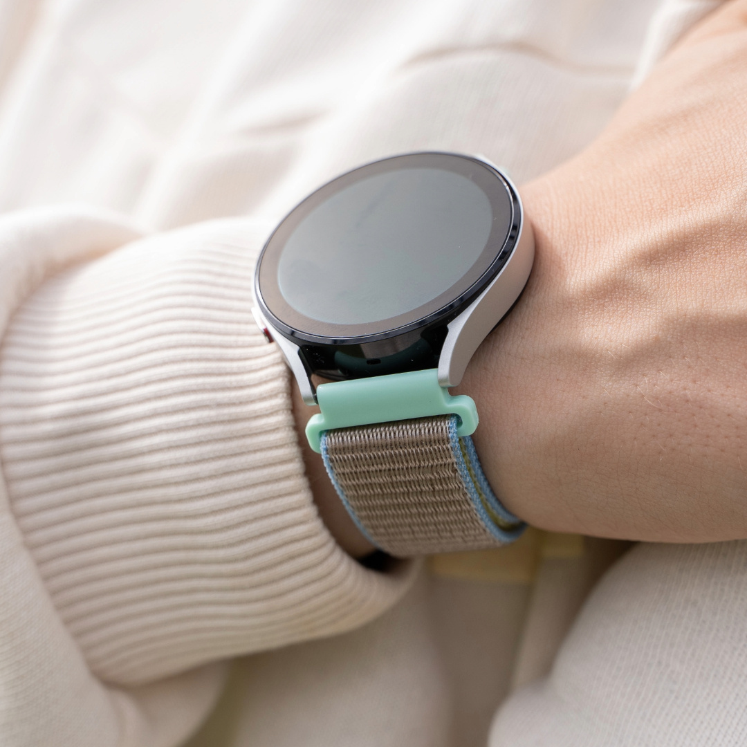 Eine Smartwatch an einem Handgelenk. Die Uhr hat ein rundes Zifferblatt und ein blau-beiges Armband.
