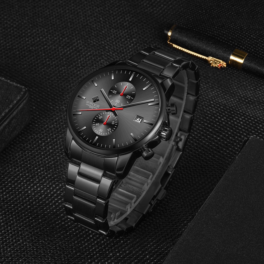 Schwarze Armbanduhr auf dunkler Oberfläche. Die Uhr hat schwarze Details und einen roten Sekundenzeiger. Ein Stift im Hintergrund.