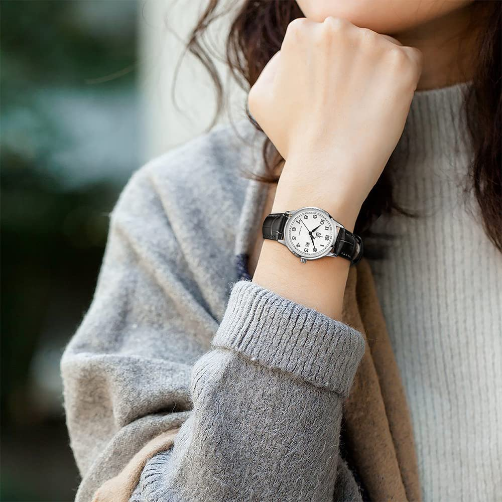 Handgelenk einer Frau mit Uhr. Uhr hat weißes Zifferblatt und schwarzes Armband.