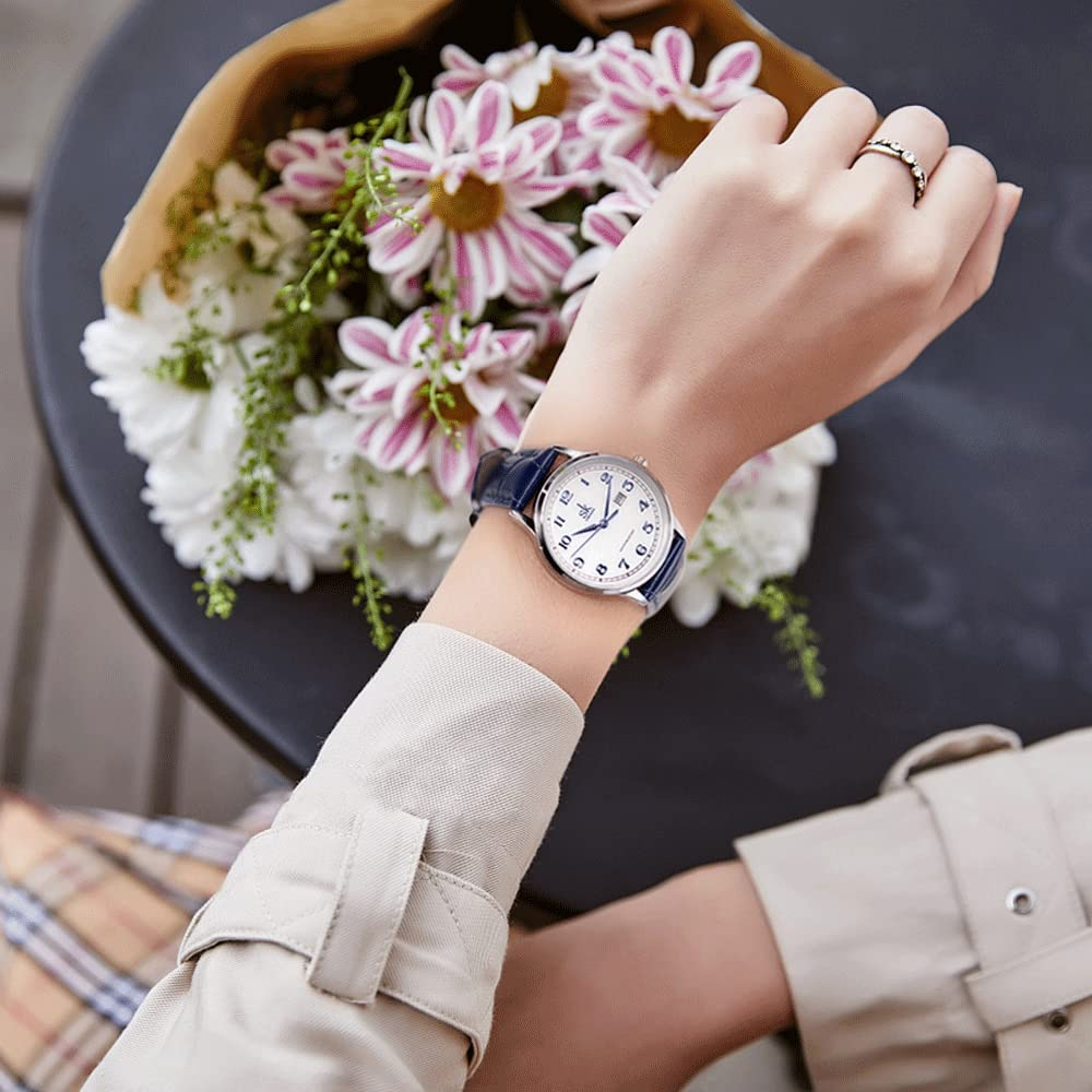 Eine Frau mit einer Uhr mit blauem Armband hält Blumen. Ein Tisch ist im Hintergrund.