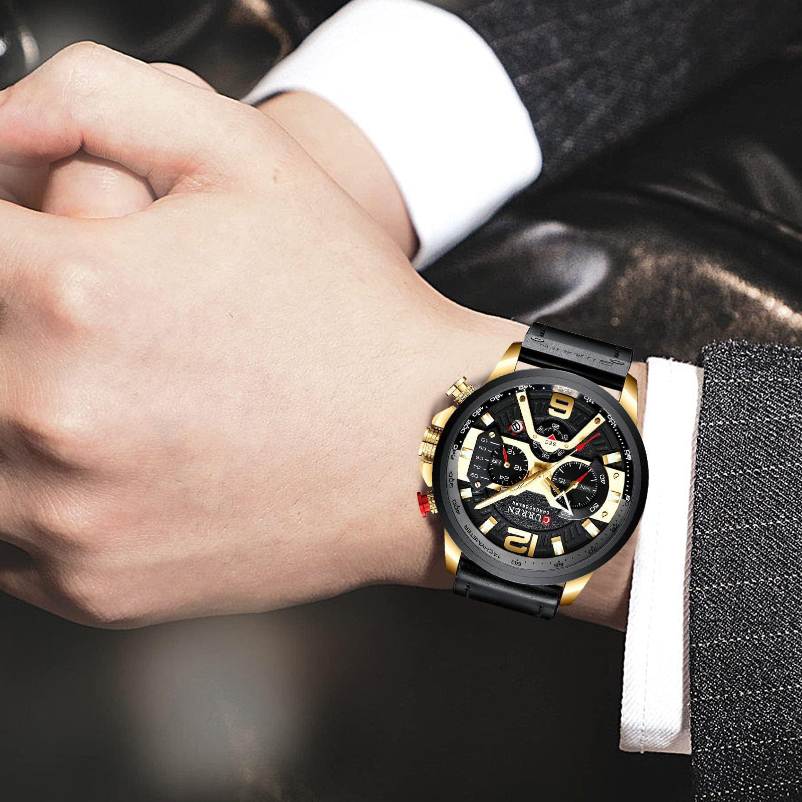 Das Handgelenk eines Mannes mit einer schwarz-goldenen Armbanduhr auf einem Anzug.