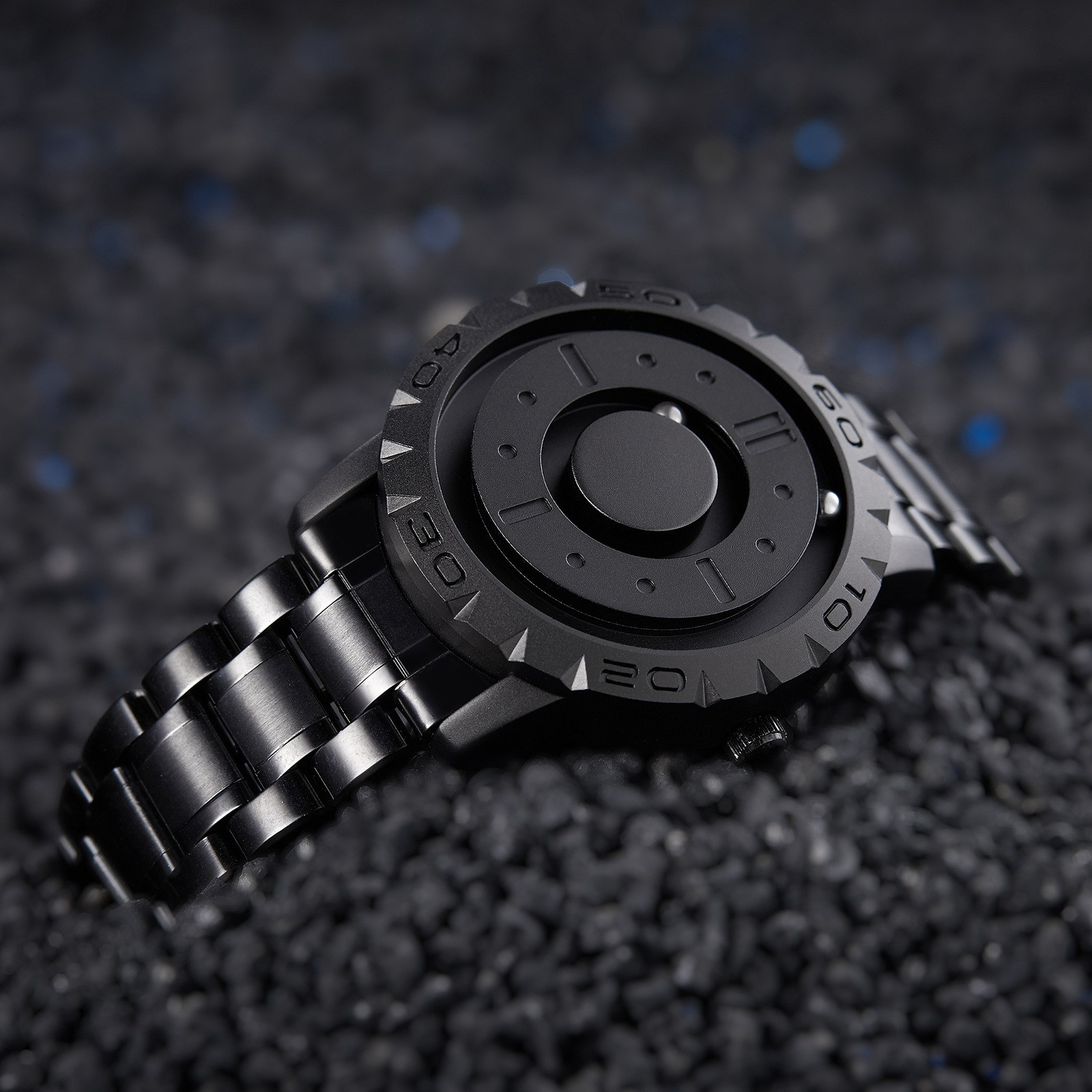 Schwarze Armbanduhr auf strukturierter Oberfläche, mit einzigartigem kreisförmigen Zifferblatt.