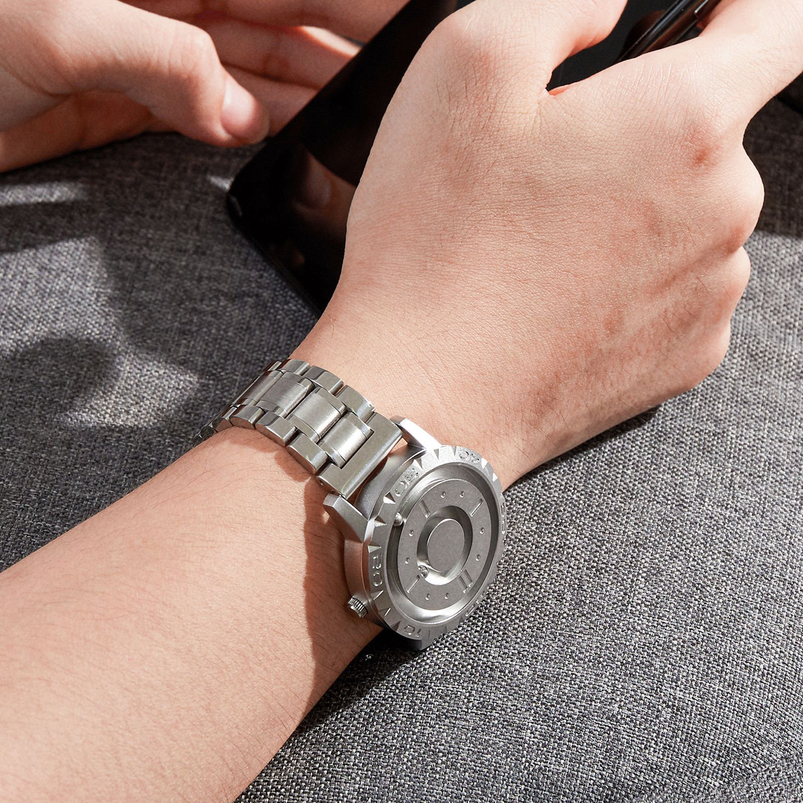 Das Handgelenk einer Person mit einer silbernen Uhr. Die Uhr hat ein kreisförmiges Design.