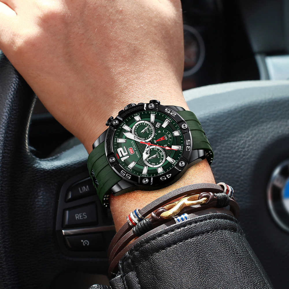 Handgelenk eines Mannes mit Uhr und Armband. Die Uhr ist grün und schwarz. Der Hintergrund ist unscharf.