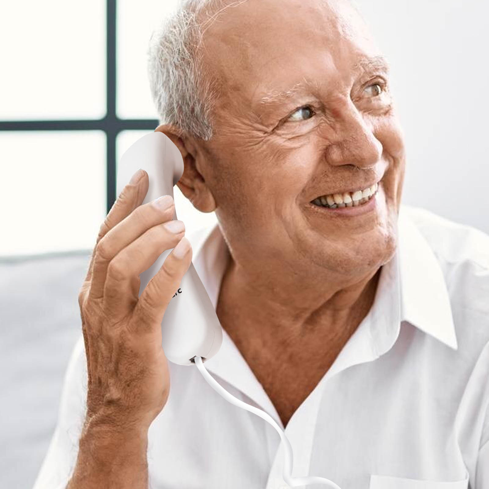 Ein älterer Mann lächelt, während er ein weißes Telefon an sein Ohr hält.