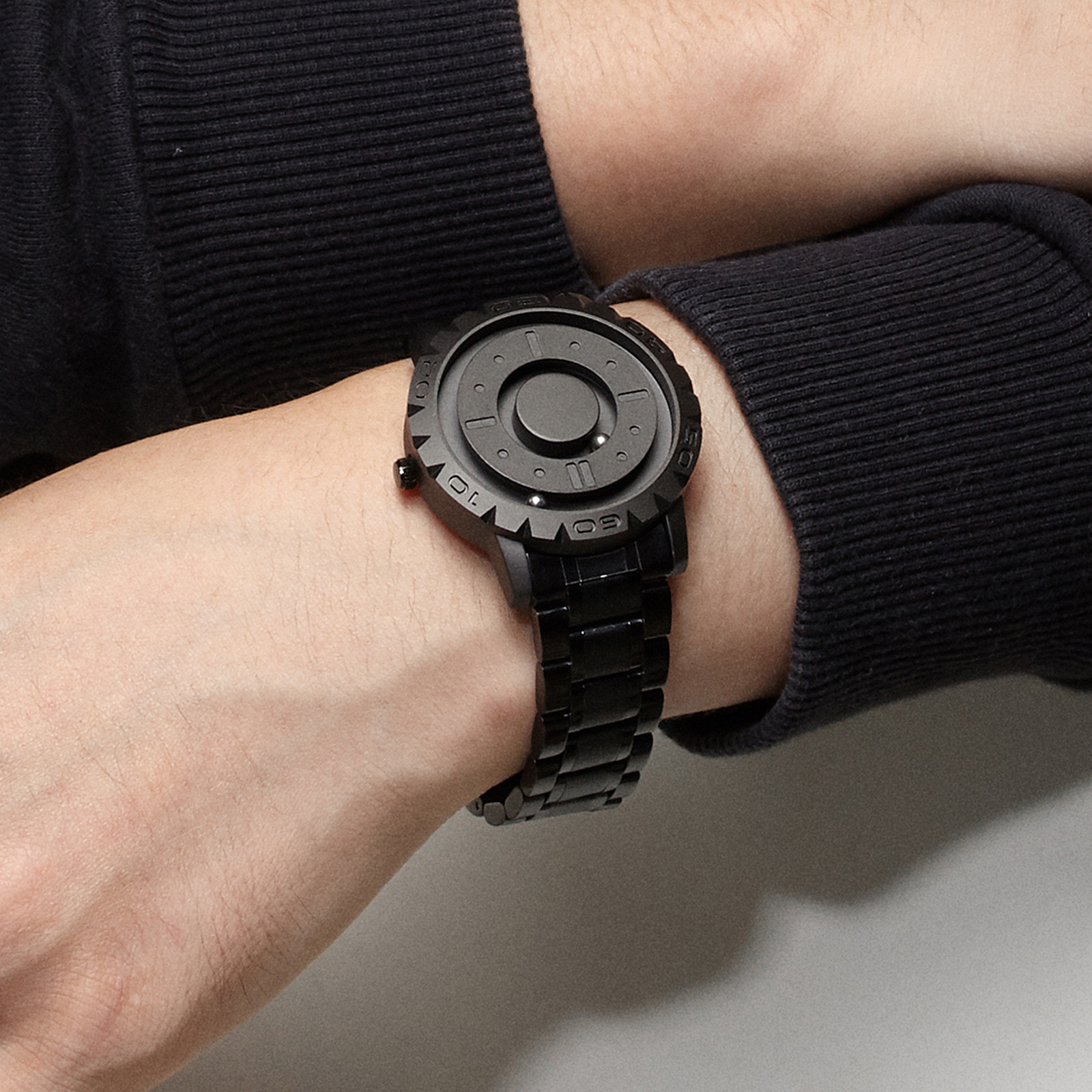 Schwarze Uhr am Handgelenk. Die Uhr hat ein schwarzes Armband und ein rundes, gemustertes Zifferblatt.