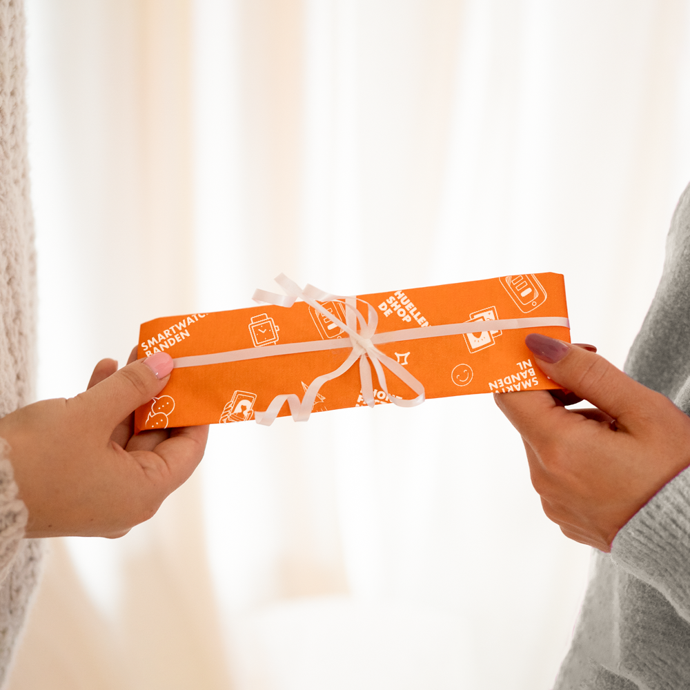 Hände halten ein verpacktes Paket. Das Paket ist orange und hat ein weißes Band. Text drauf.