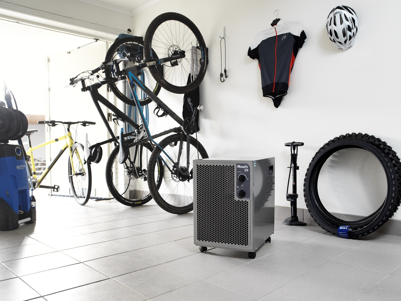 Eine Garage mit Fahrrädern, einer grauen Maschine und einem Fahrradreifen. Eine weiße Wand mit hängenden Gegenständen.