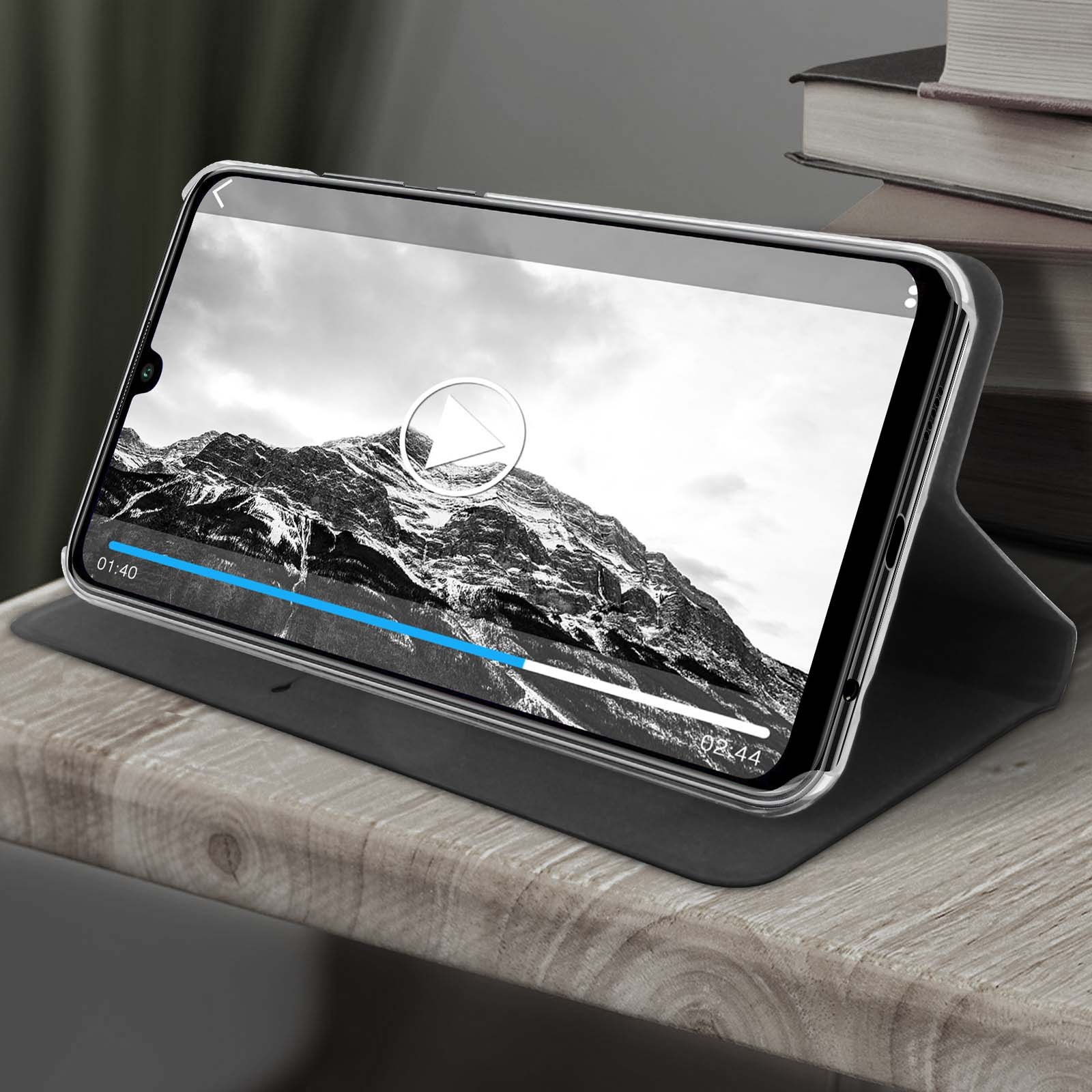 Tablet su supporto che riproduce video, montagne sullo sfondo, libri.