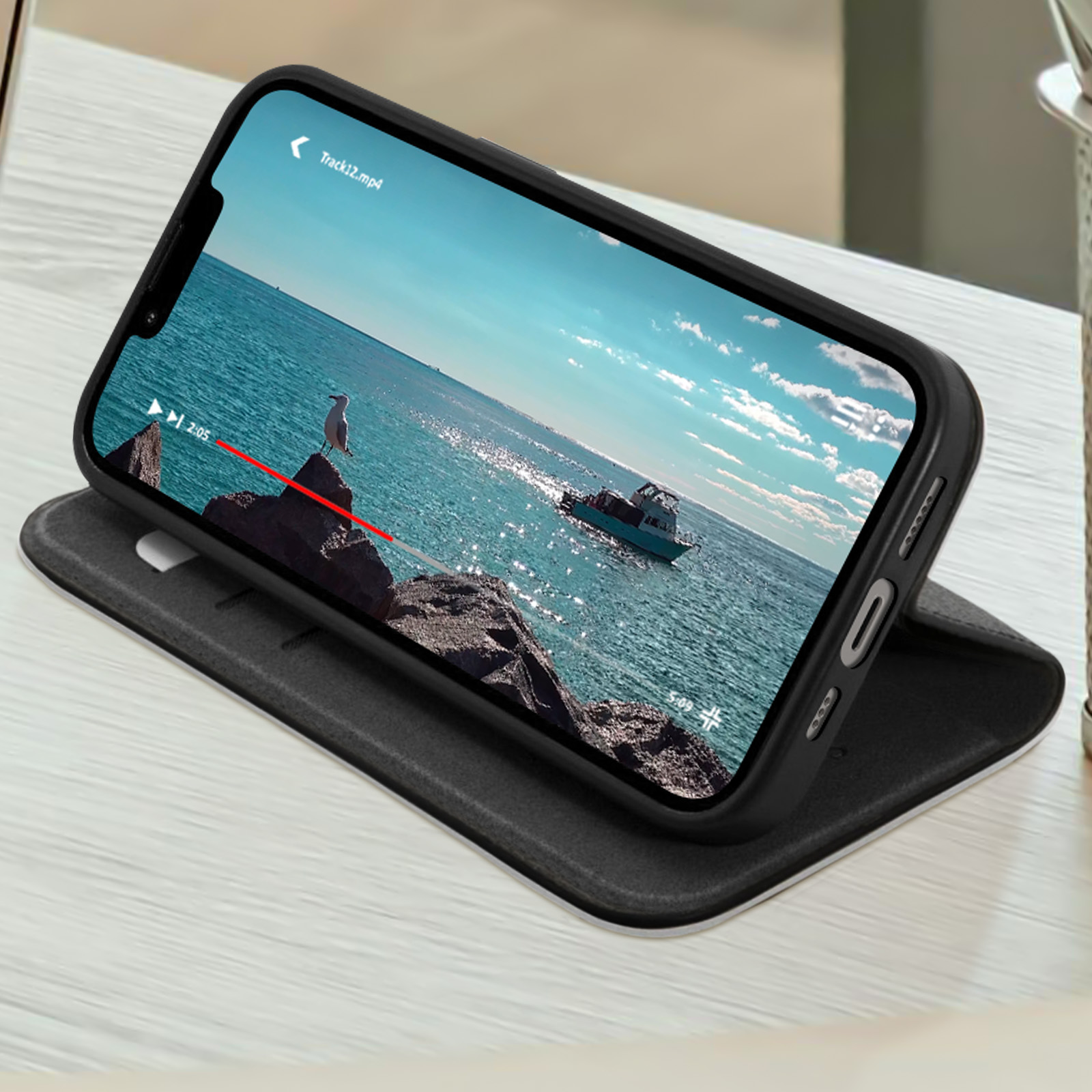 Telefono che mostra un video su un supporto. Il telefono è su un tavolo. Lo sfondo è un mare luminoso.