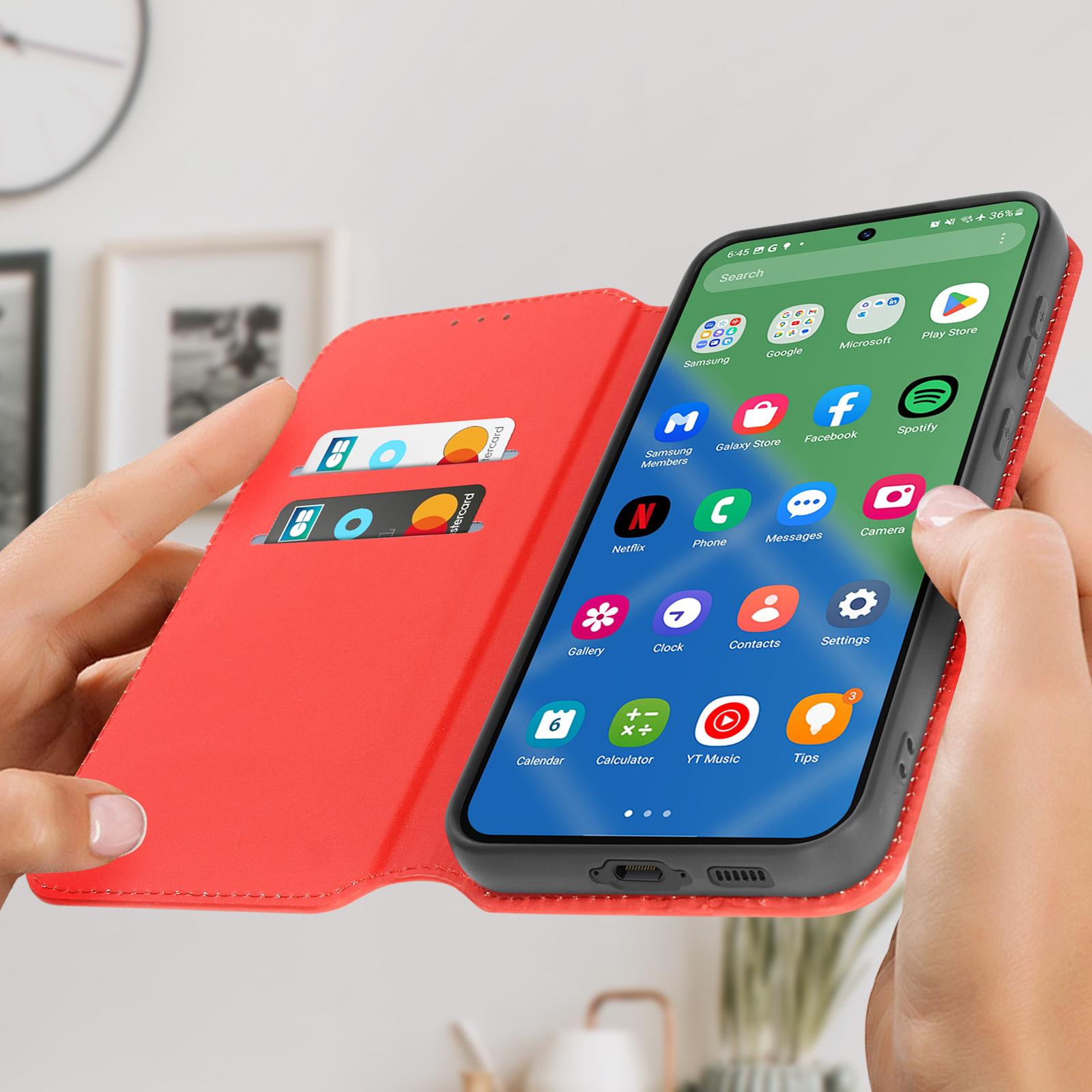 Mani che tengono aperta la custodia rossa, mostrando lo schermo del telefono con le app. Sfondo con orologio e cornice.