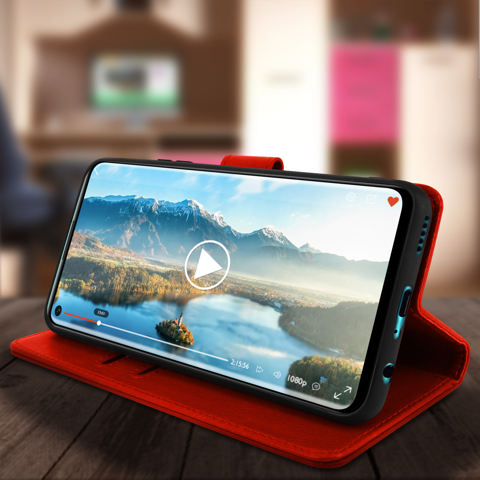 Telefono in custodia rossa che mostra un video. Tavolo in legno, sfondo sfocato.