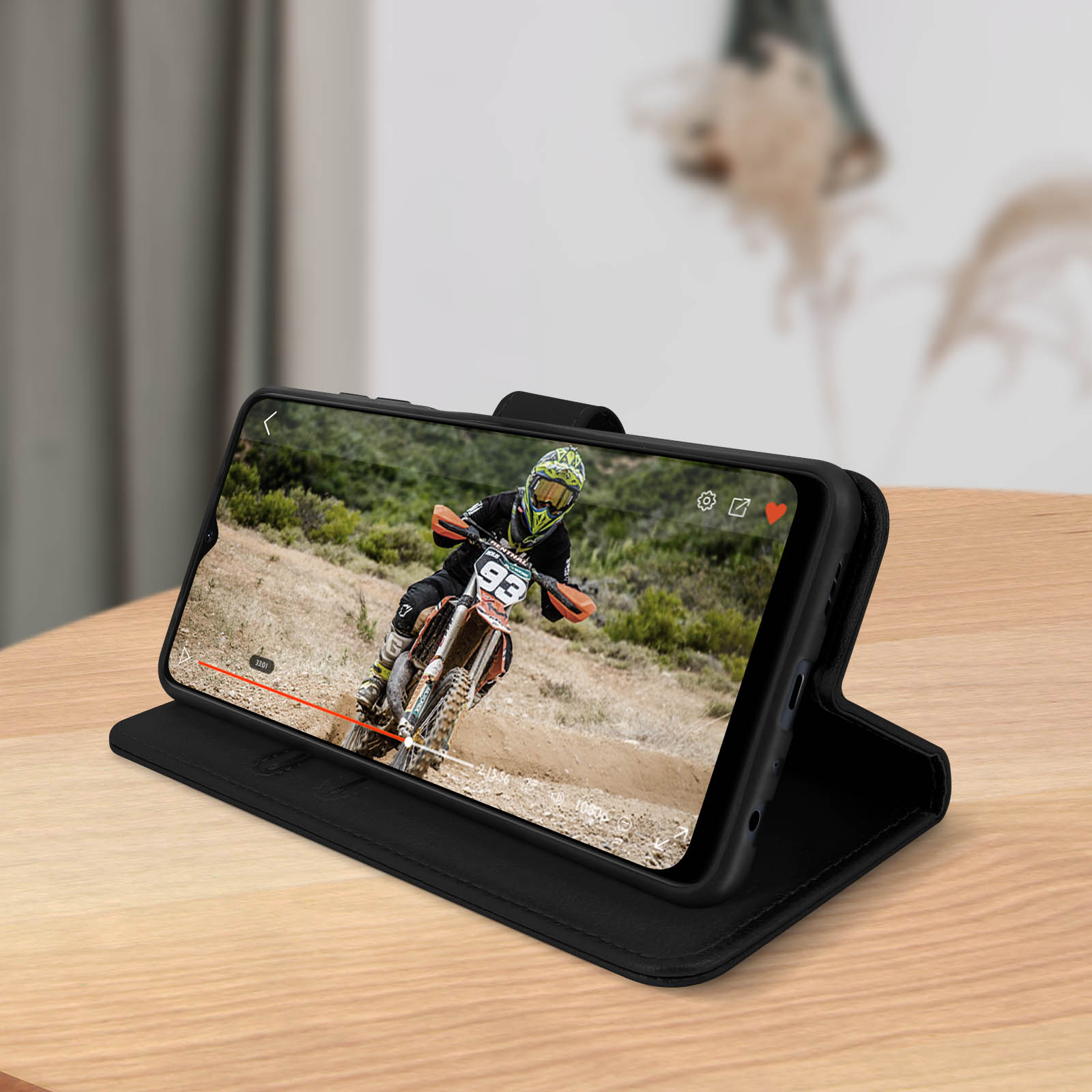 Custodia per telefono nera con un telefono che mostra un video di una gara di motocross, su un tavolo di legno.