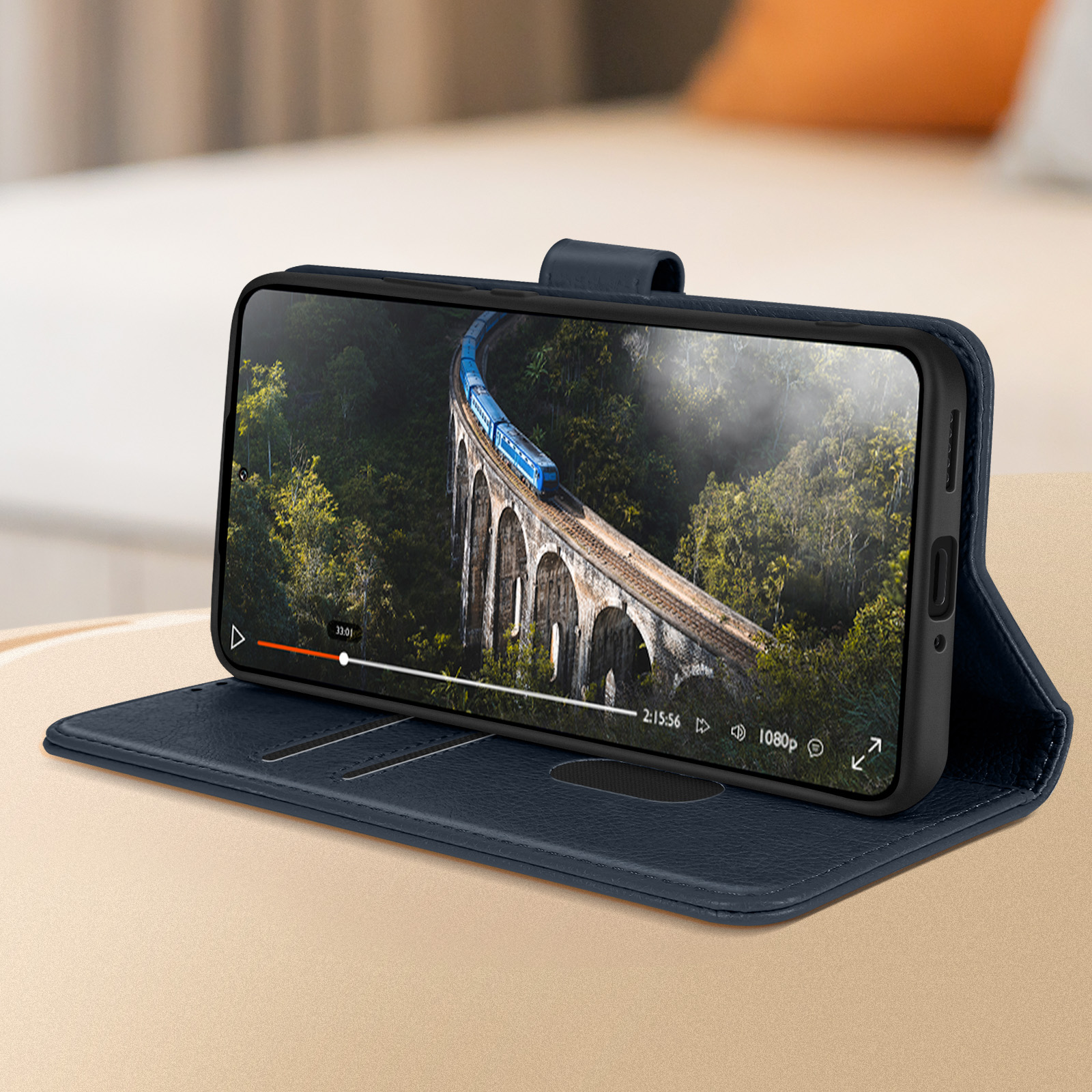 Telefon in blauer Hülle zeigt Video eines Zuges auf Brücke, auf beiger Oberfläche.