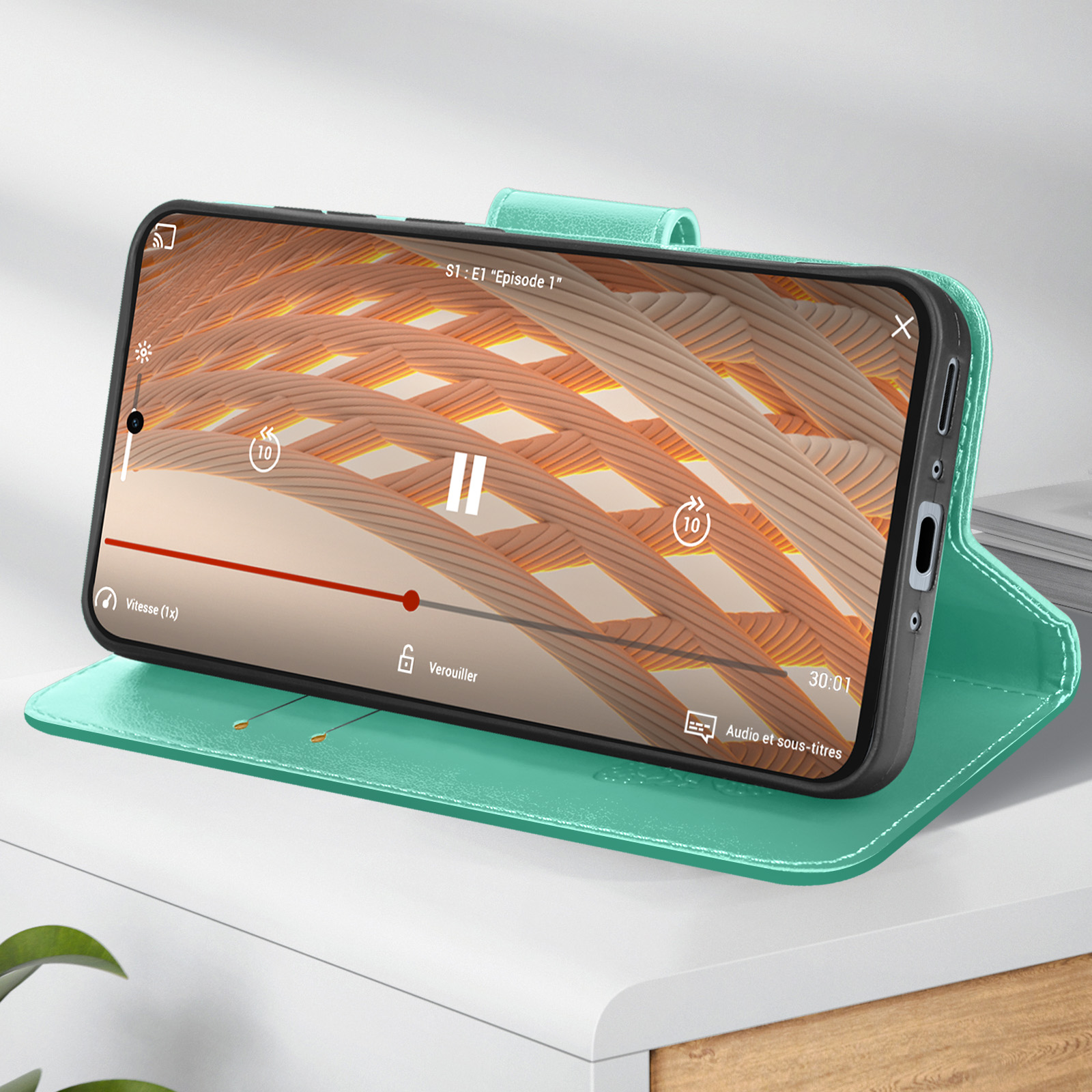 Telefon in grüner Hülle spielt Video ab. Weißer Tisch. Bildschirm zeigt Video-Interface.