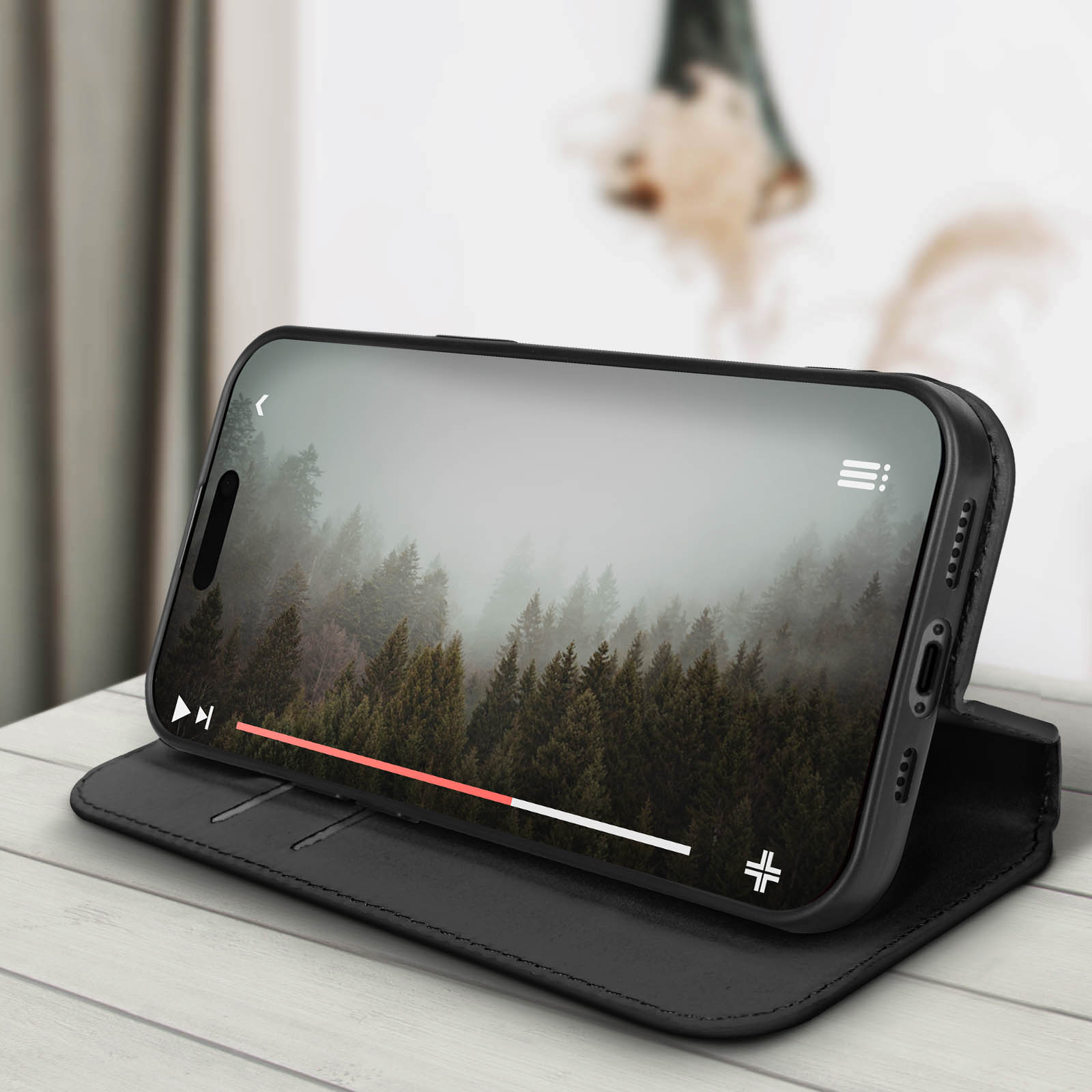 Uno smartphone mostra un video di una foresta. È appoggiato su una custodia in pelle nera.