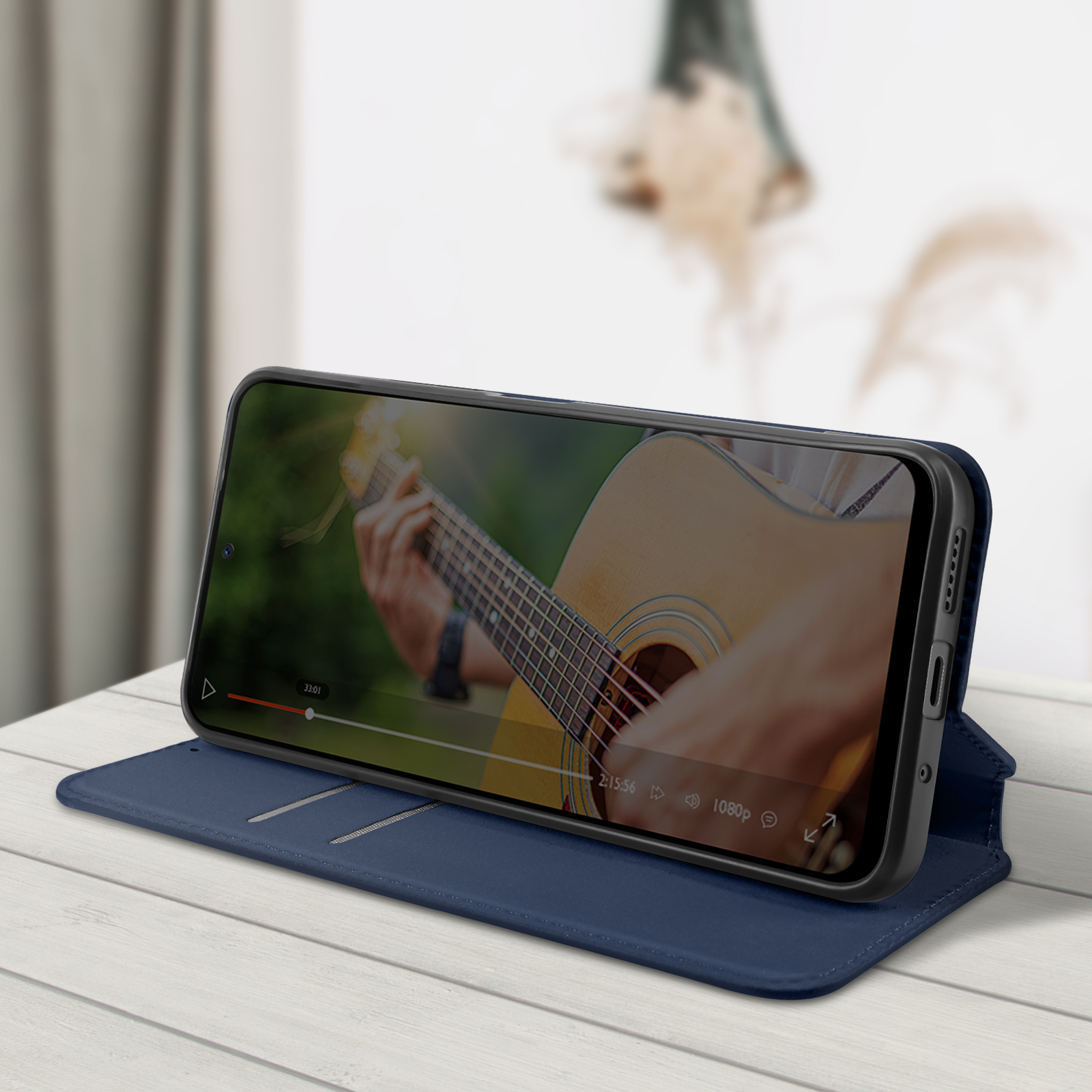Telefon in Etui, zeigt Video eines Mannes, der Gitarre spielt. Das Etui ist geöffnet und aufgestellt.