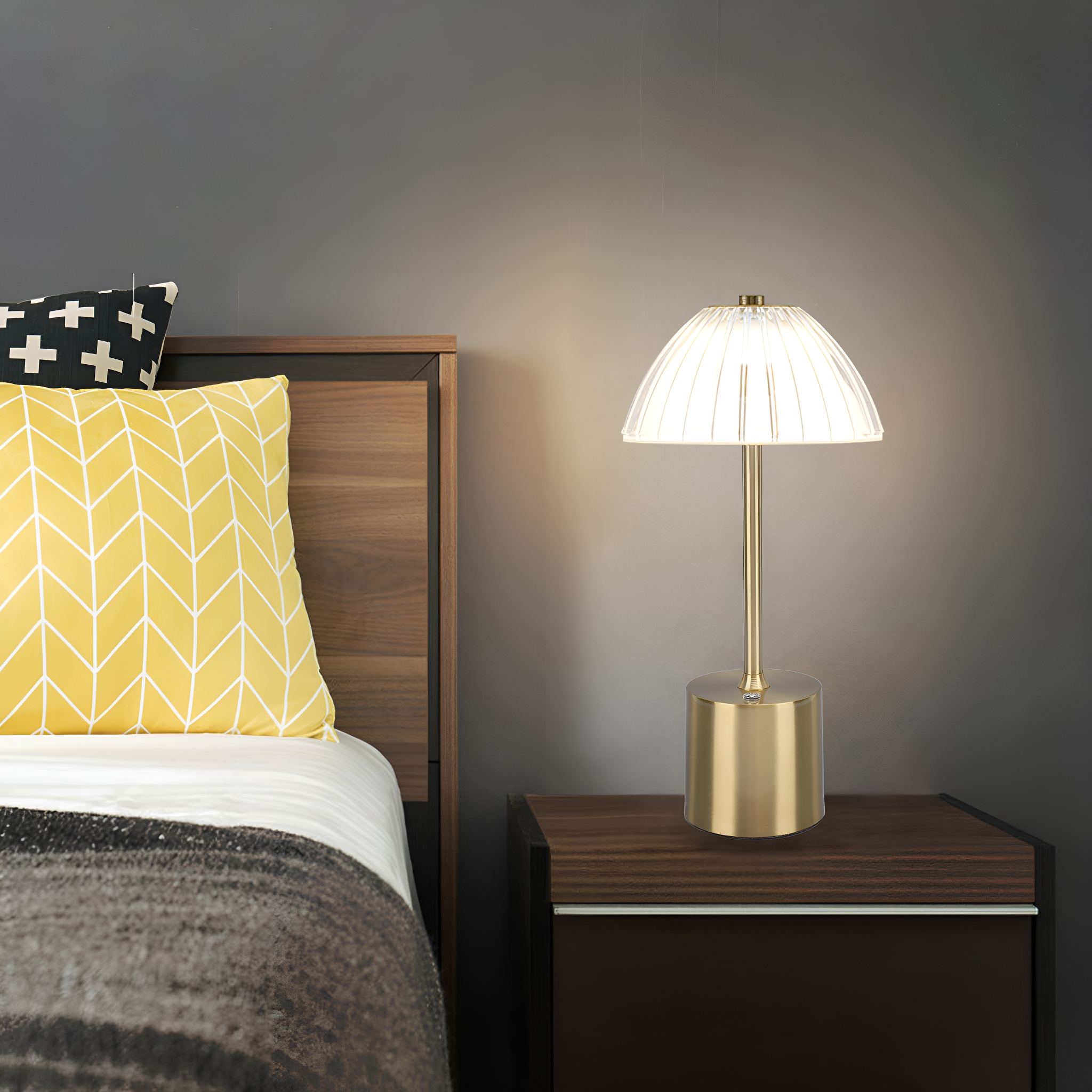 Nachttischlampe mit goldenem Fuß und weißem, geripptem Schirm, neben einem Bett.