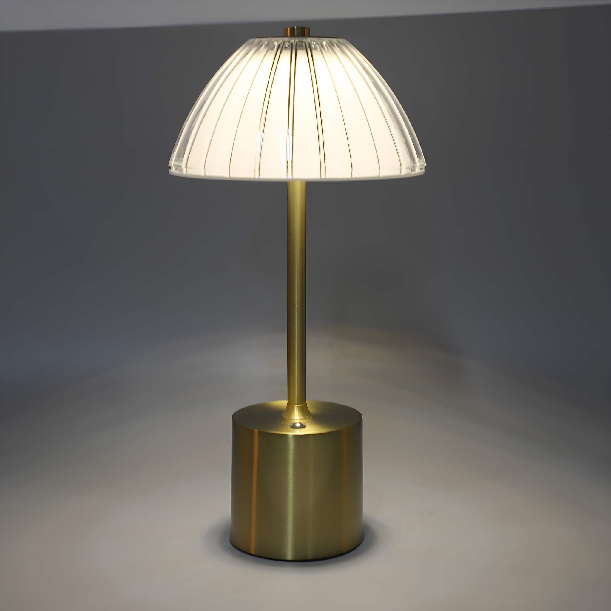 Eine messingfarbene Tischlampe mit plissiertem, weißem Lampenschirm, mit Licht an.