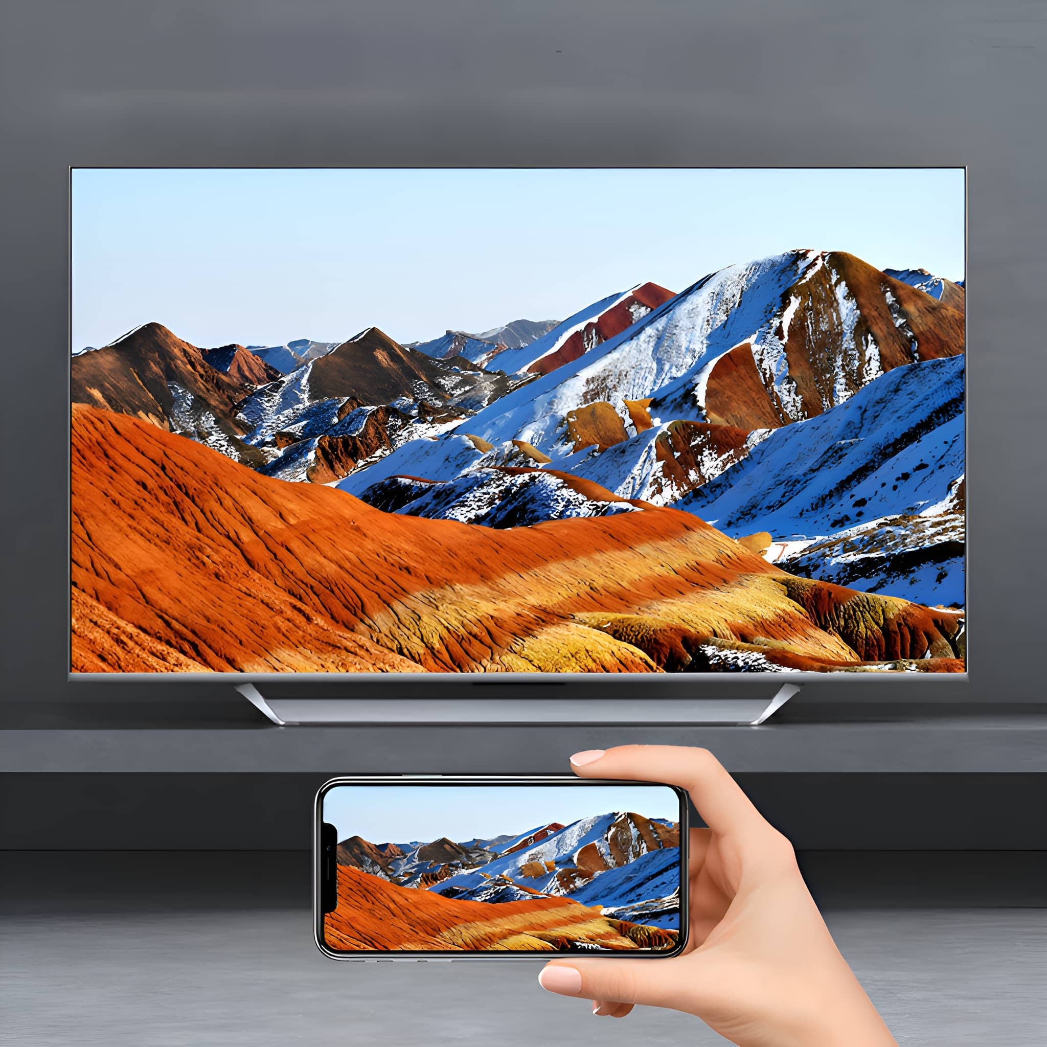 Ein großer Fernseher zeigt eine farbenfrohe Berglandschaft. Eine Hand hält ein Telefon mit derselben Szene.
