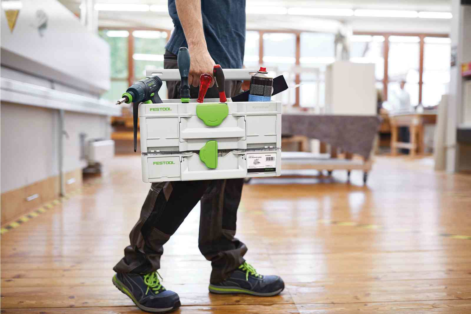 Un uomo in un'officina porta una cassetta degli attrezzi bianca piena di utensili.