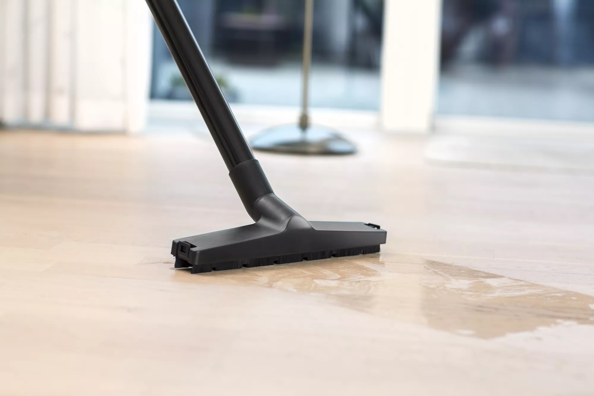 Una boquilla de aspiradora limpiando un suelo de madera clara, agua en el suelo.