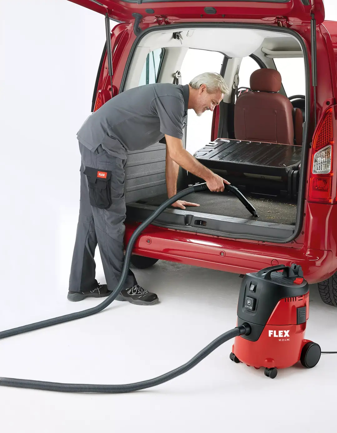 Uomo che aspira l'interno di un bagagliaio rosso con un aspirapolvere Flex.