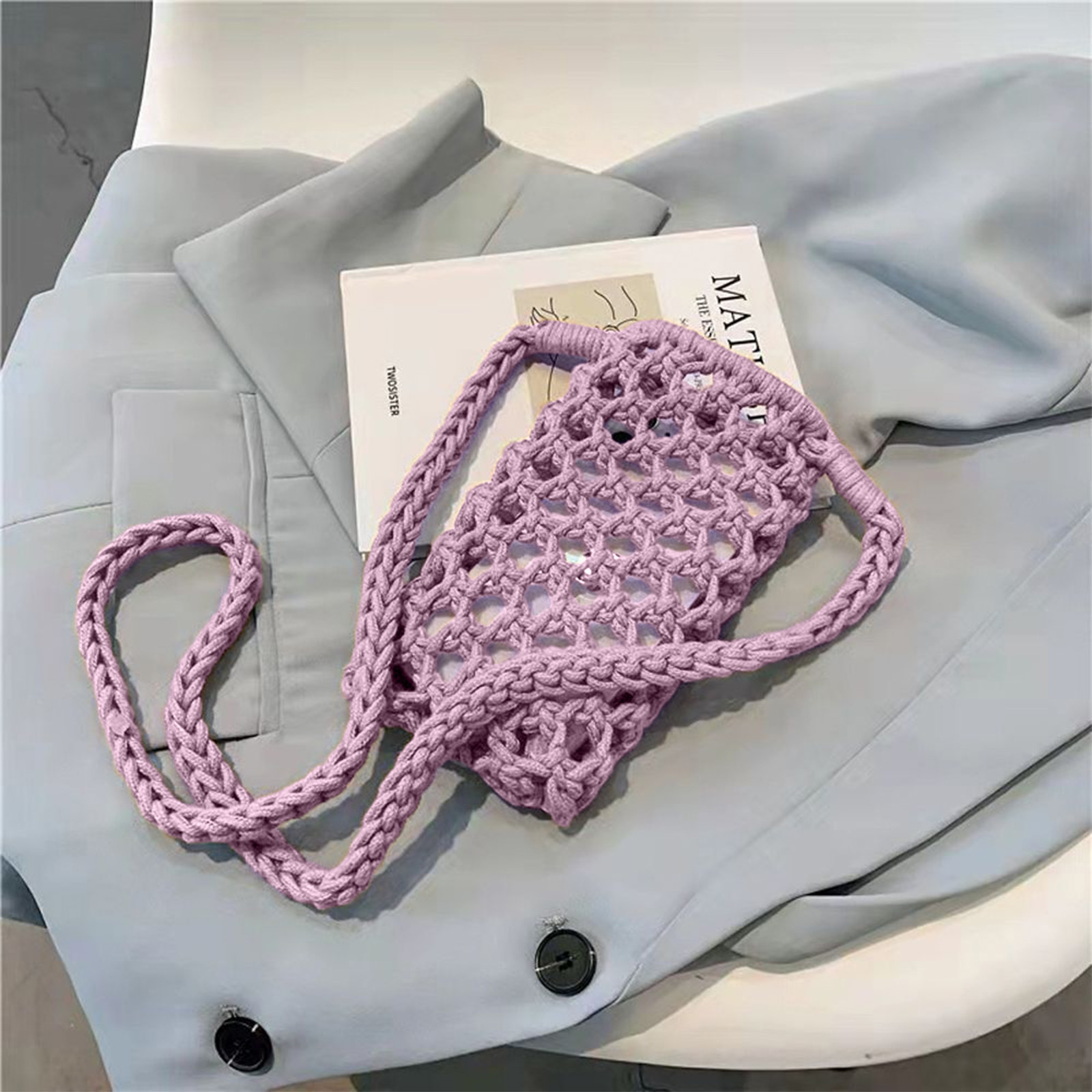Una borsa per telefono lilla a maglia è appesa a una giacca azzurra, con un libro a lato.