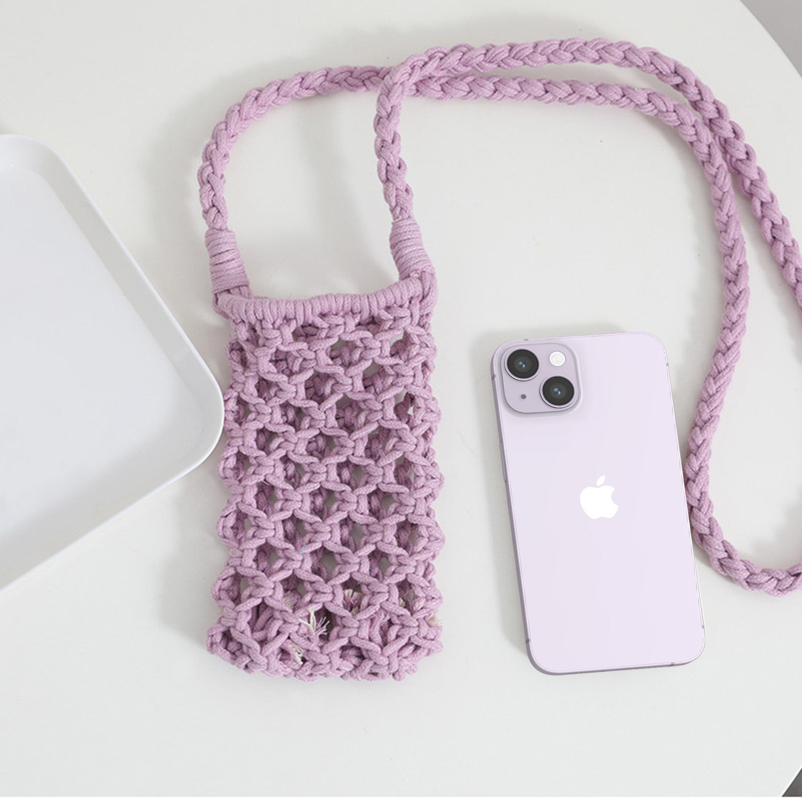 Telefono viola e porta telefono in macramè su una superficie bianca. Un vassoio bianco a sinistra.