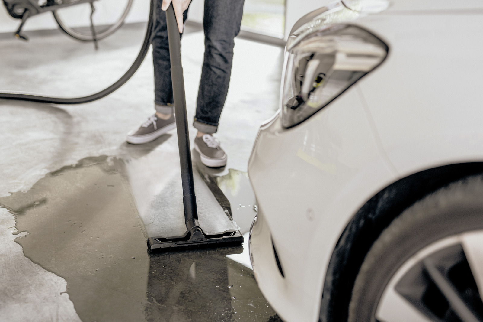 Una persona che aspira un pavimento bagnato del garage accanto a un'auto bianca.