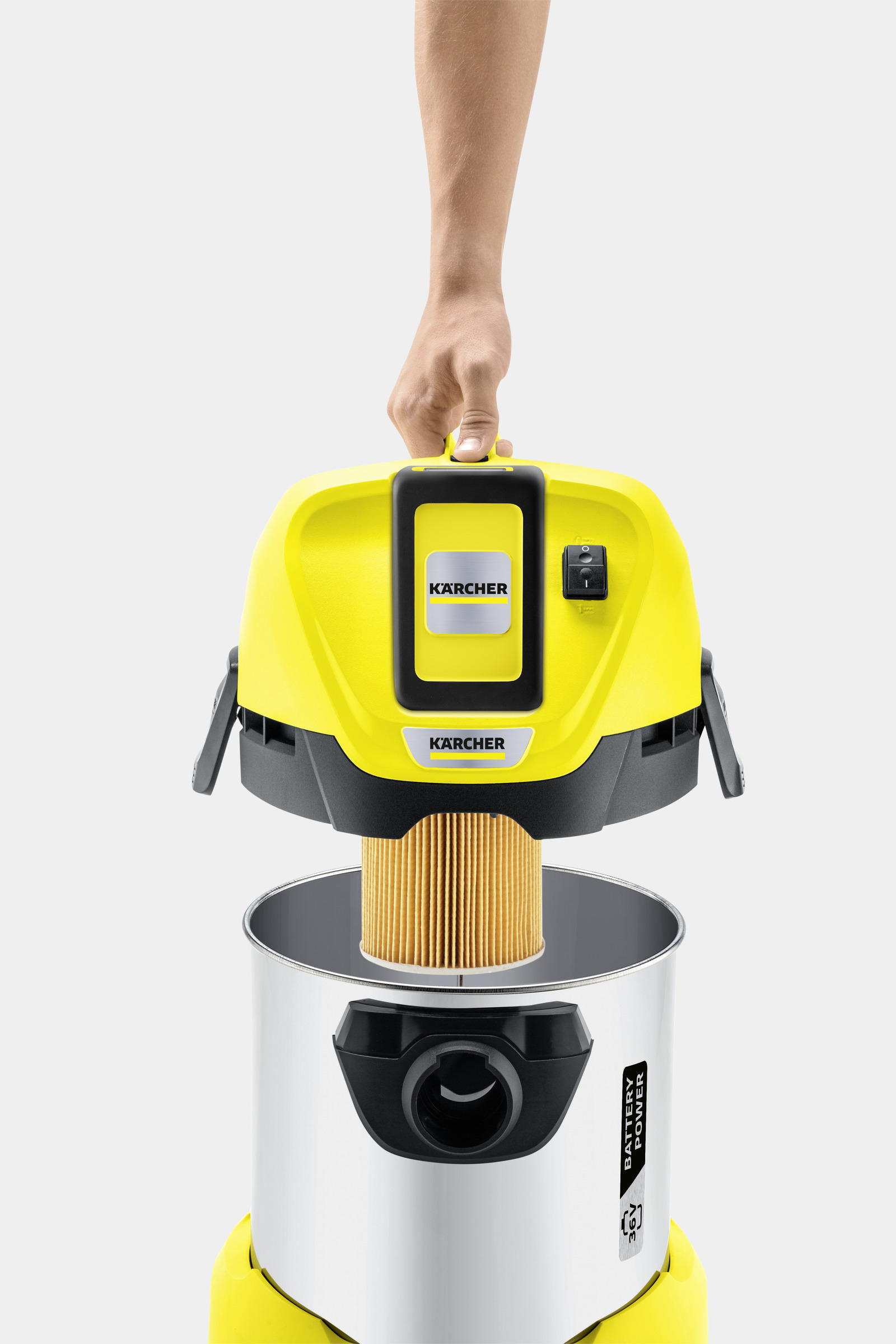 Main tenant le haut d'un aspirateur jaune, filtre visible, sur fond clair.