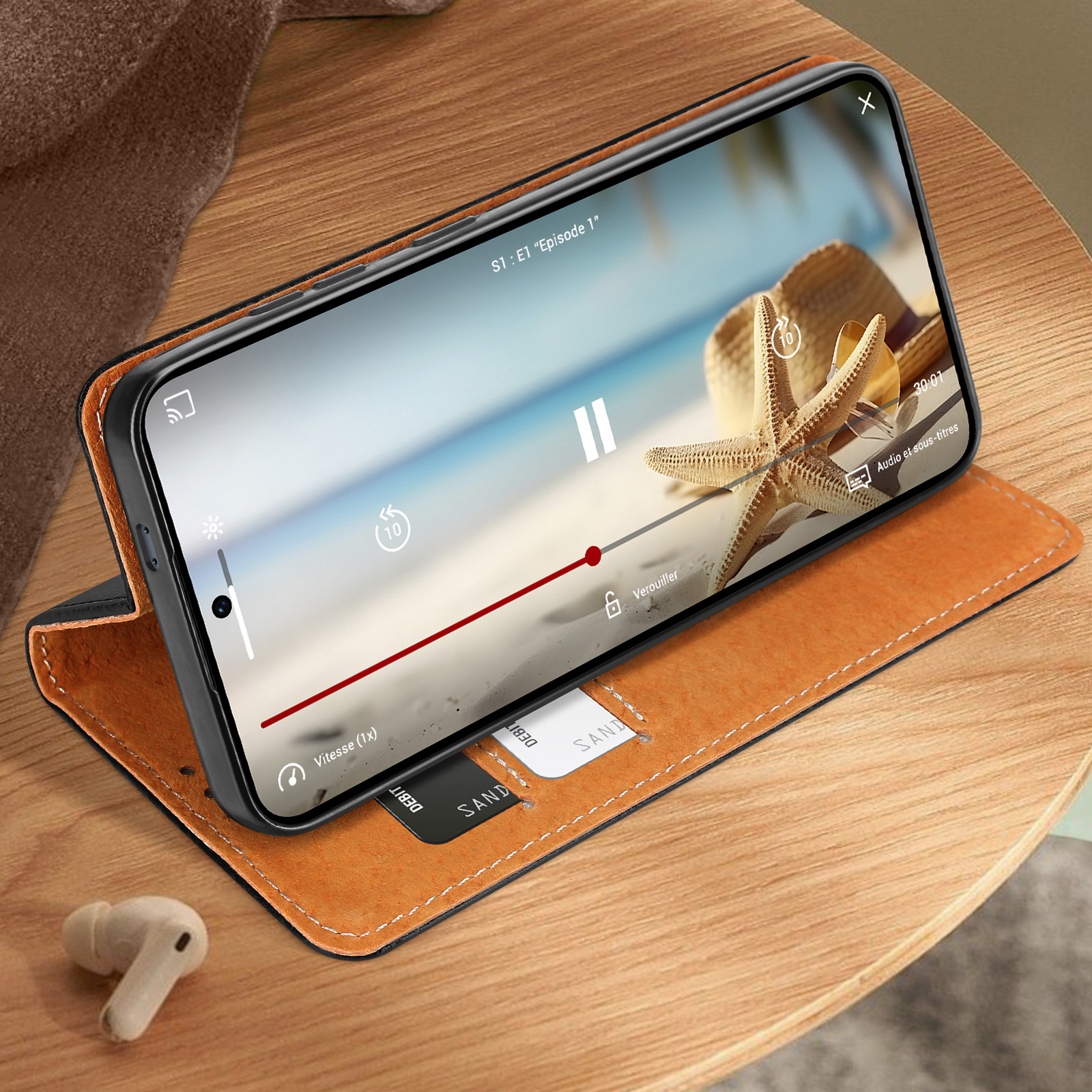 Telefono in una custodia, riproduce un video sullo schermo. Include un cappello, una stella marina e uno sfondo di spiaggia.