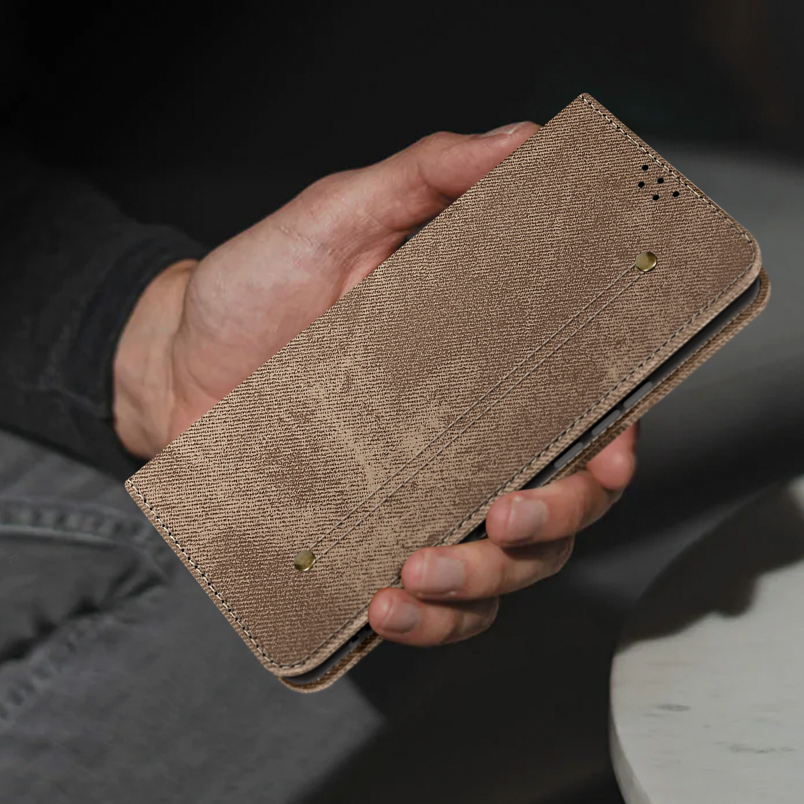 Una mano che tiene una custodia marrone con superficie strutturata. La custodia è chiusa e dal design minimalista.