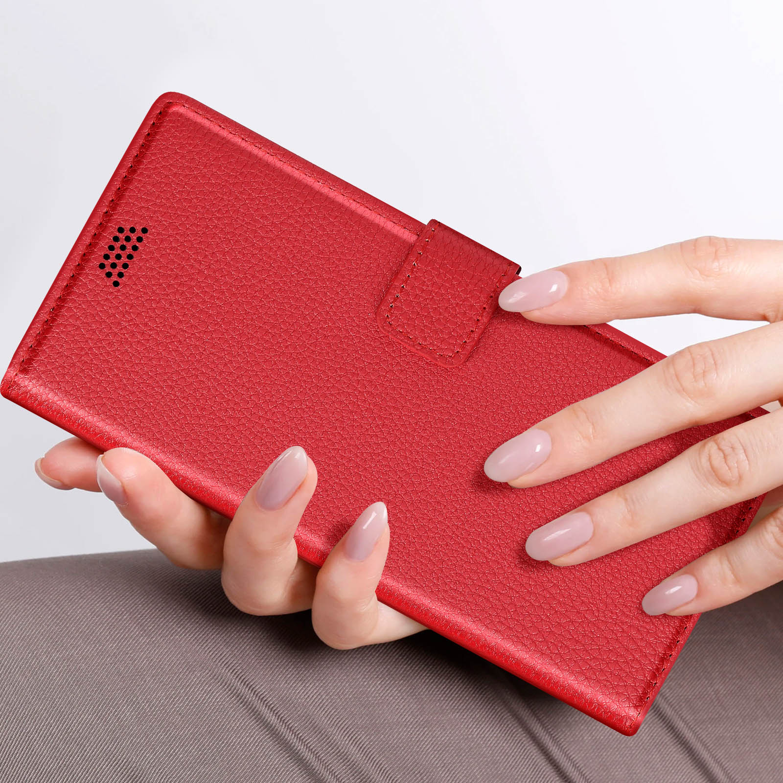 Una mano che tiene una custodia per telefono in pelle rossa, la custodia è chiusa con una linguetta.