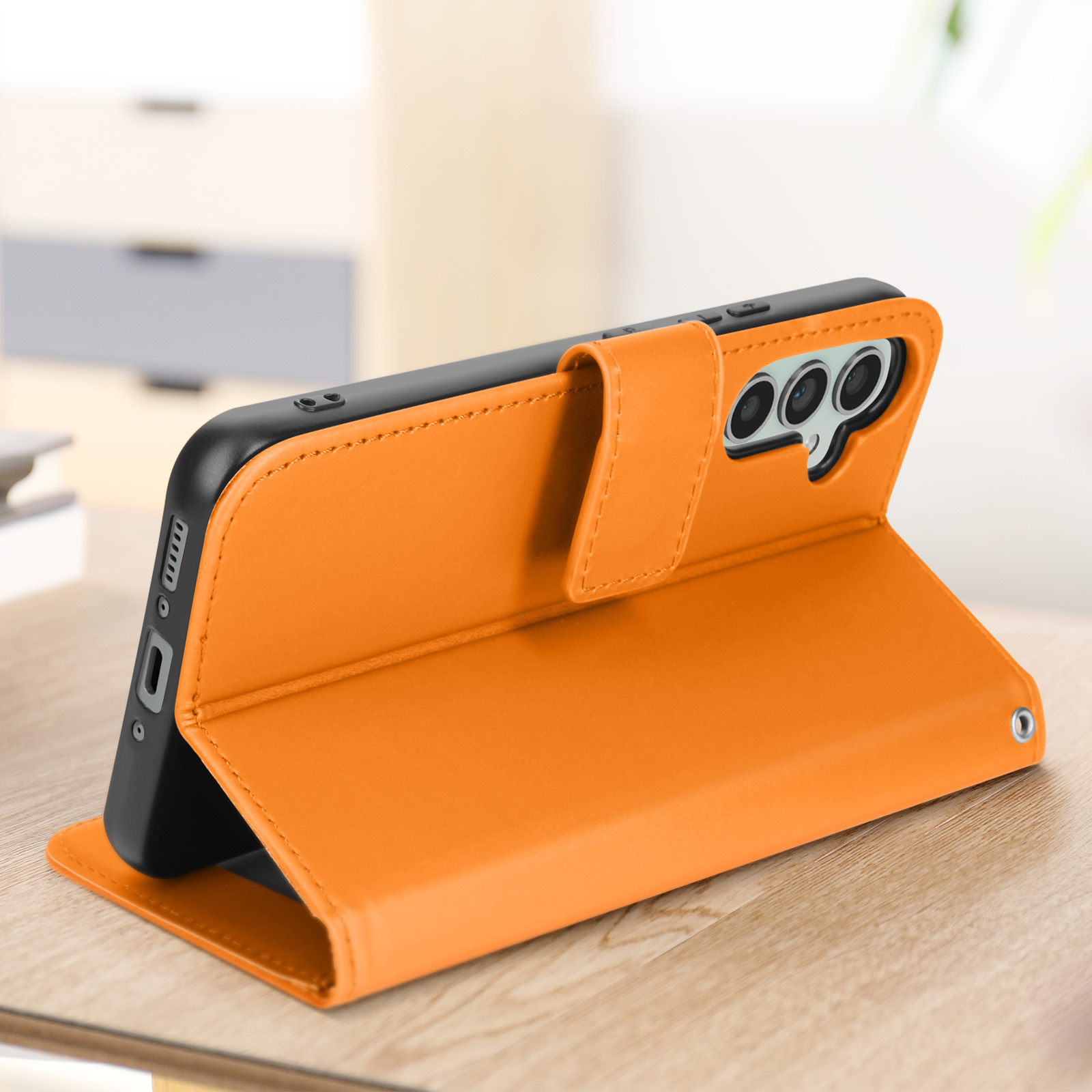 Custodia arancione aperta, telefono dentro. Tre fotocamere sul telefono. Su un tavolo di legno in una stanza.