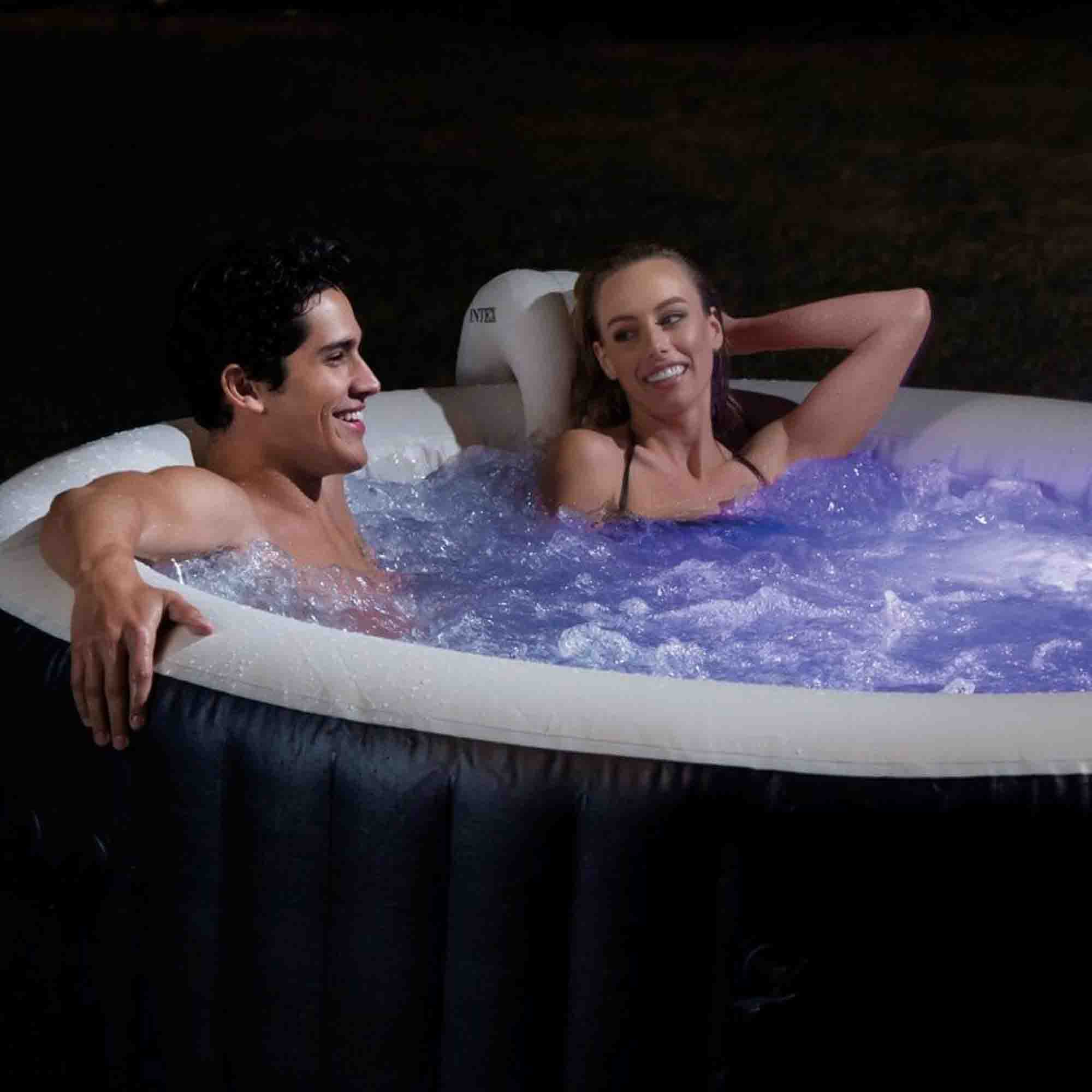 Ein lächelndes Paar in einem beleuchteten Whirlpool bei Nacht mit Blasen.