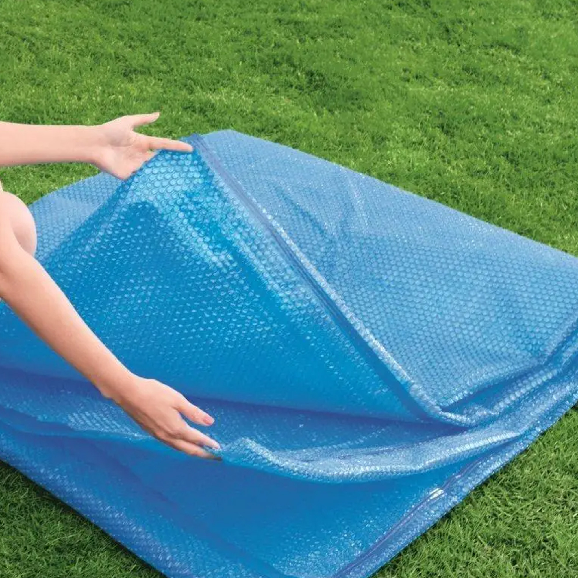 Mani che aprono una copertura blu a bolle su erba verde. La copertura è piegata.