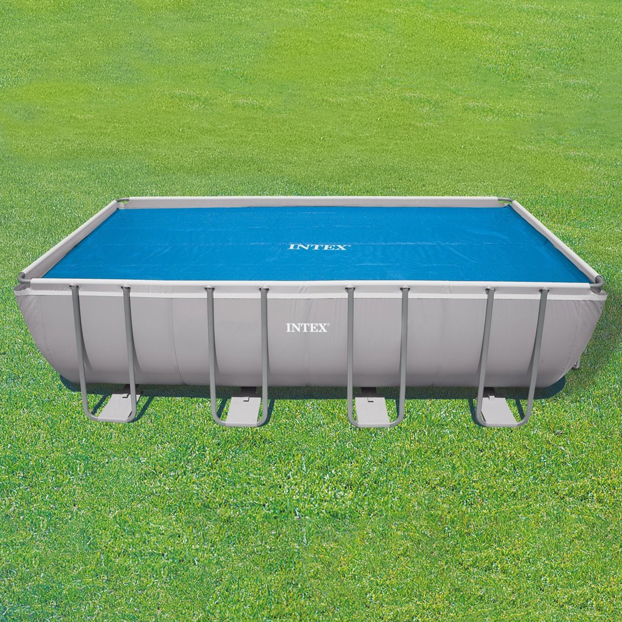 Piscina fuori terra rettangolare con copertura blu su erba verde. La piscina è grigia.